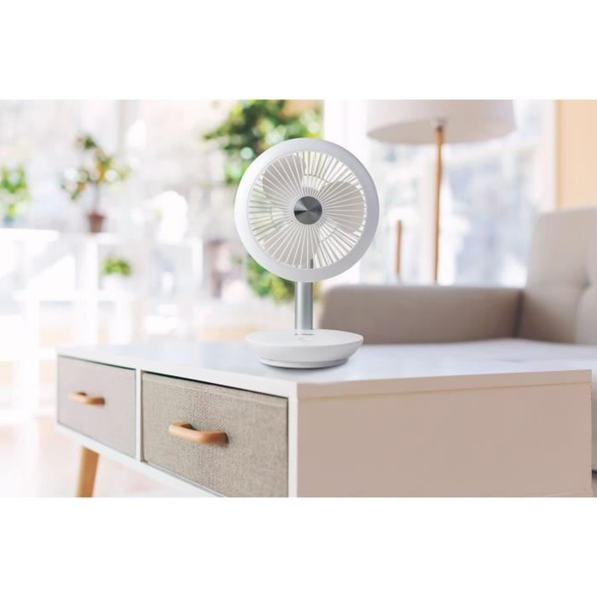 Ein kleiner weißer Ventilator steht auf einem weißen Tisch mit Schubladen. Im Hintergrund ist ein Sofa.