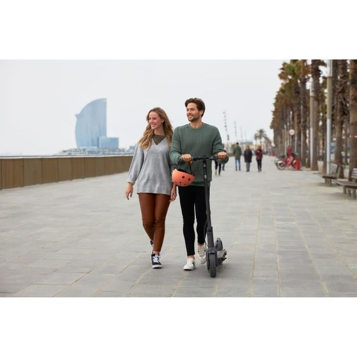 Un uomo e una donna passeggiano con uno scooter su un lungomare.