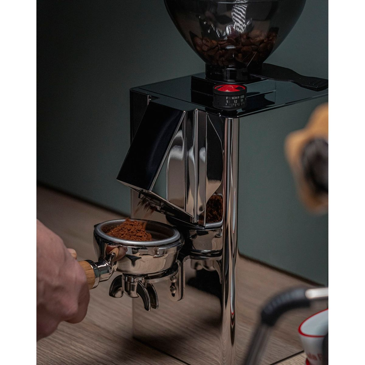 Un macinacaffè cromato macina il caffè in un portafiltro su un tavolo di legno.