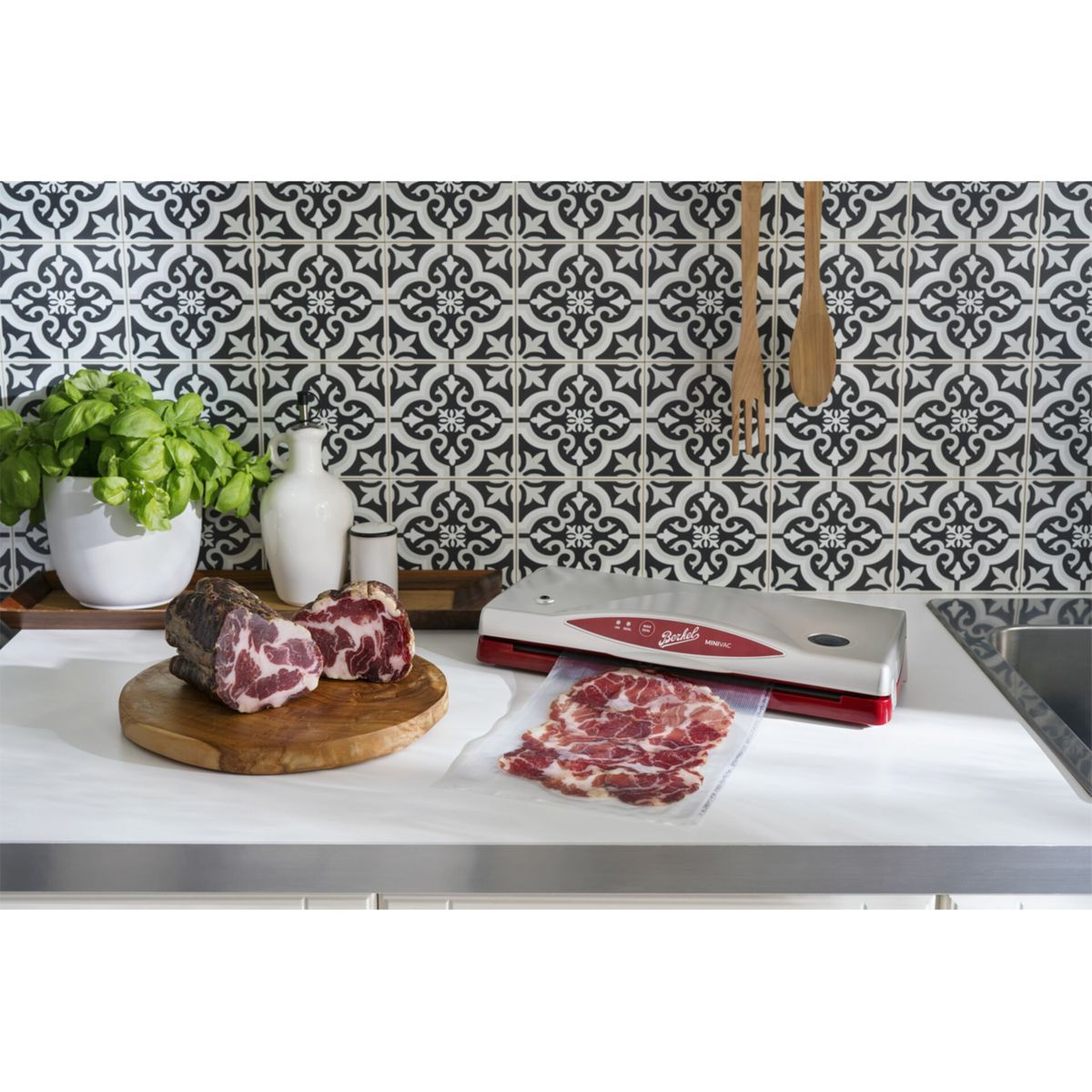 Macchina sottovuoto argento con bordo rosso, sigilla carne a fette sul piano cucina.