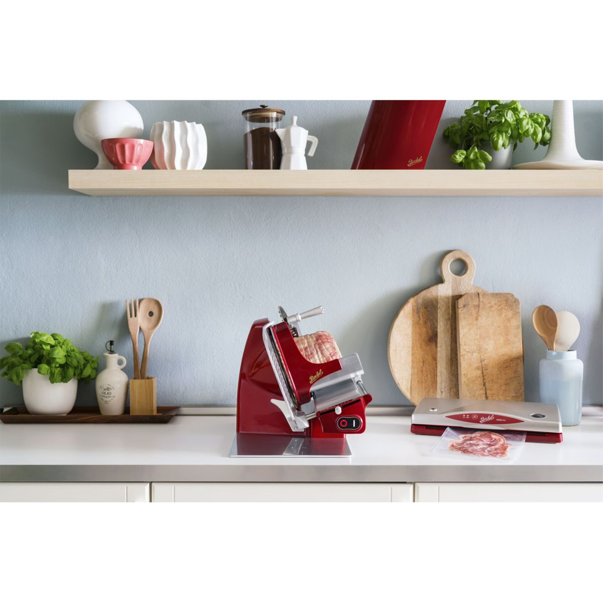 Una affettatrice rossa e una macchina sottovuoto su un bancone da cucina con piante e decorazioni.
