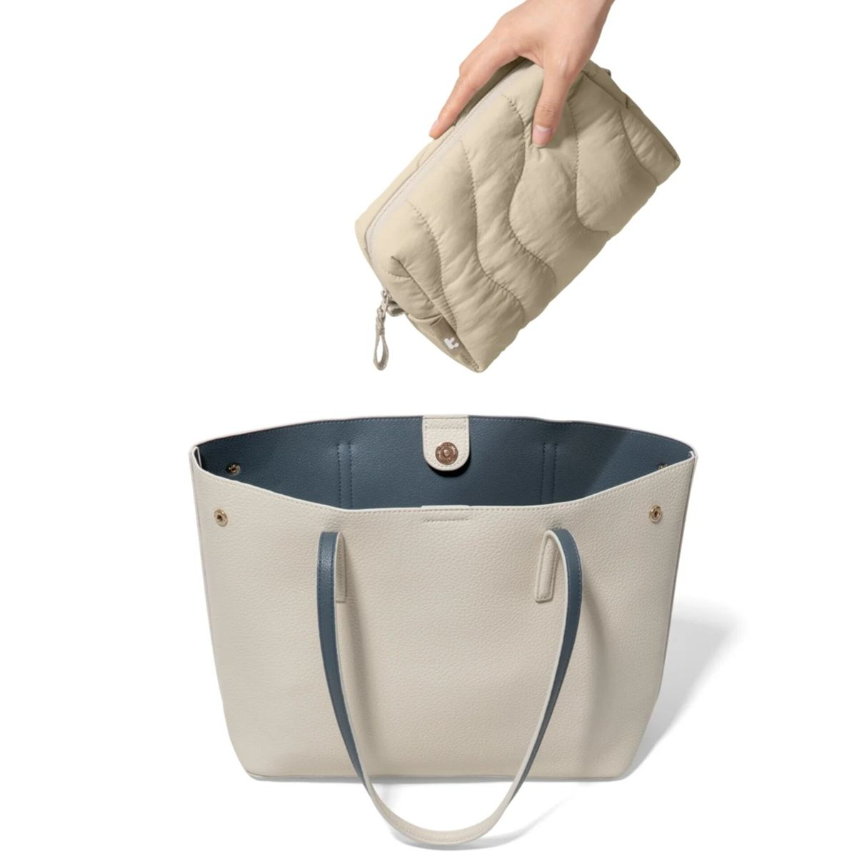 Eine Hand hält eine gesteppte beige Kosmetiktasche über eine cremefarbene Tasche mit blauen Henkeln.