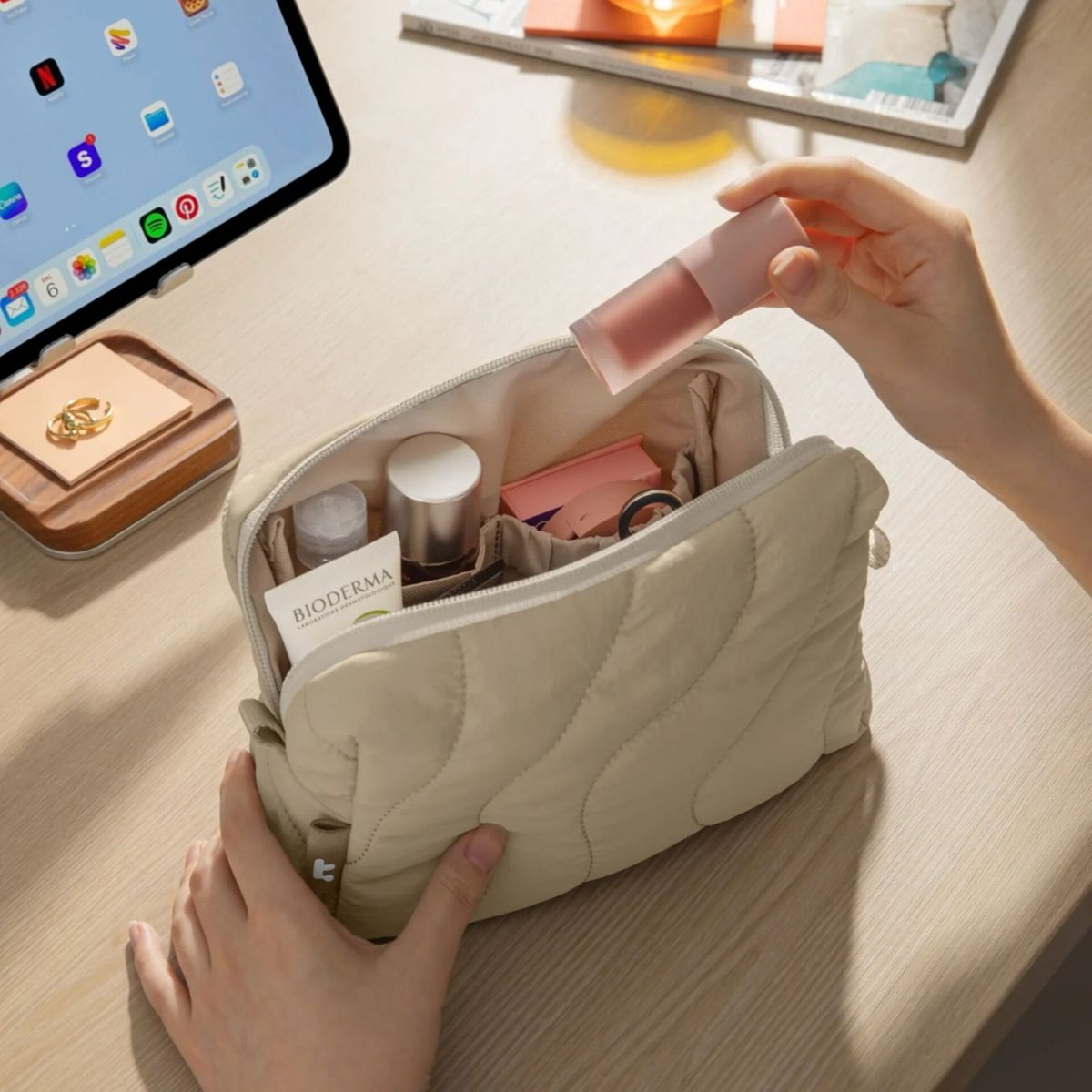 Eine Hand legt einen Lippenstift in eine offene Kosmetiktasche mit Kosmetika.
