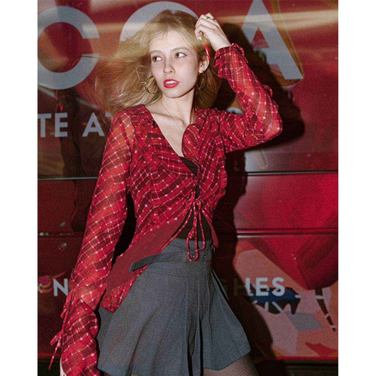 Giovane donna bionda con top a quadri rosso e gonna grigia.