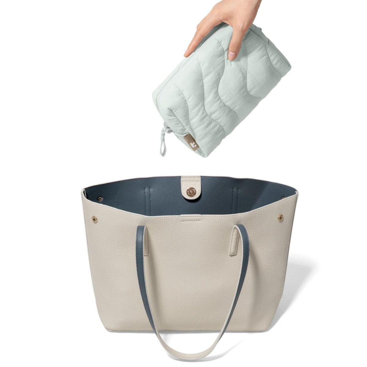 Eine Hand hält eine hellgrüne gesteppte Tasche über eine beigefarbene Tasche mit blauem Futter.