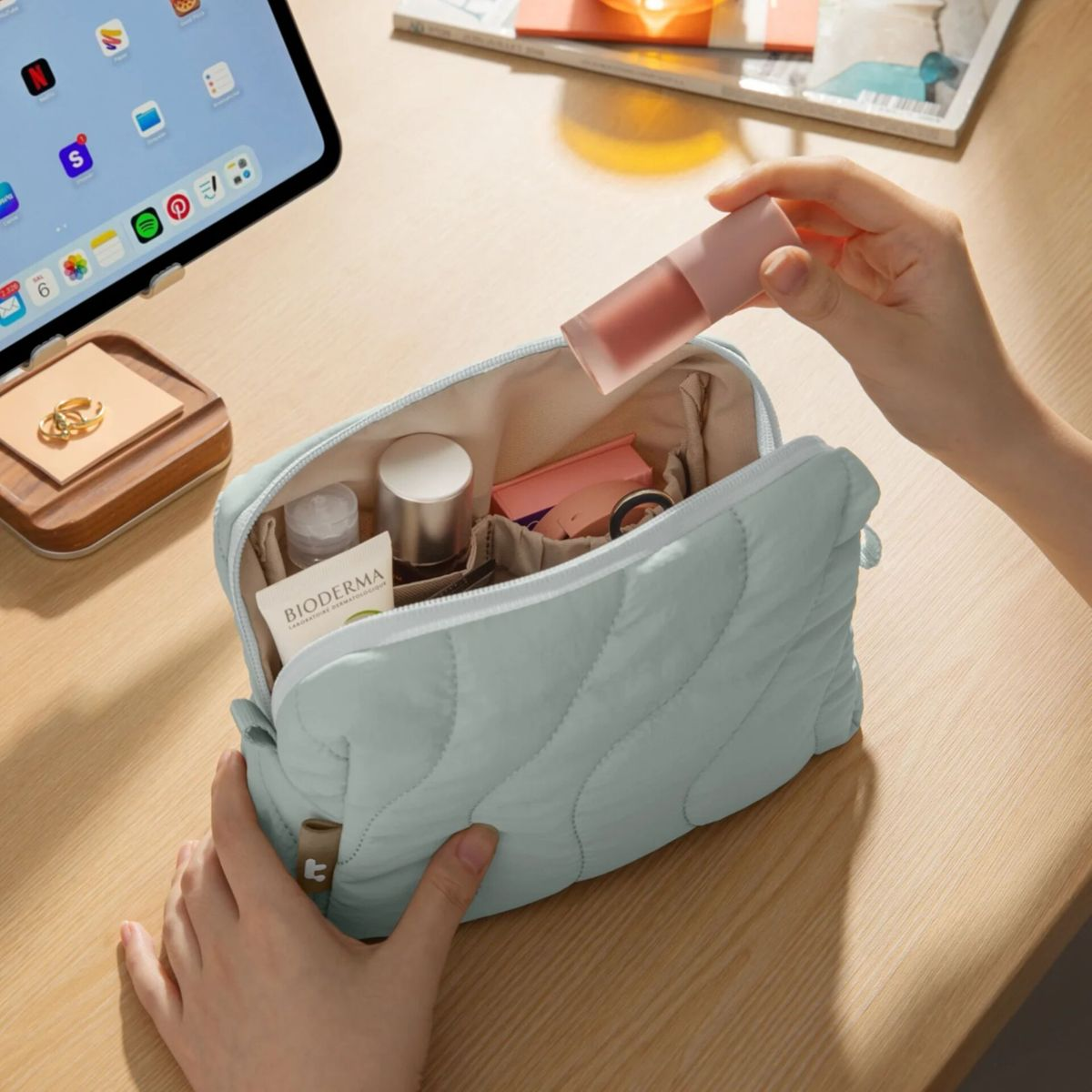 Eine Hand legt einen Lippenstift in eine geöffnete, hellgrüne Kosmetiktasche.