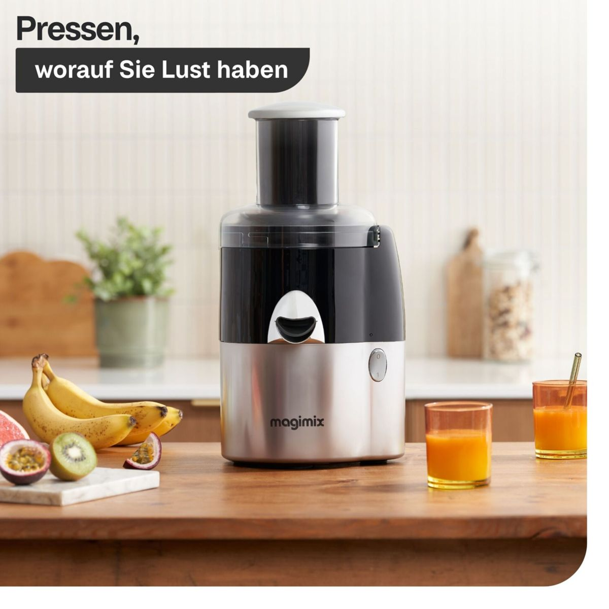 Ein Entsafter mit Obst wie Bananen und Kiwi daneben, zwei Gläser Saft.
