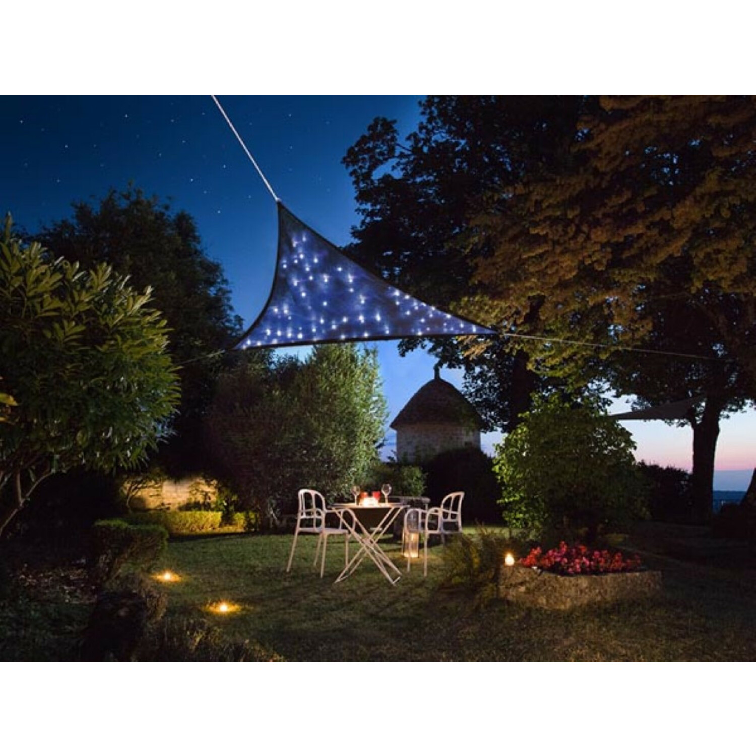 Una vela parasole illuminata sopra un tavolo da giardino con sedie di notte.