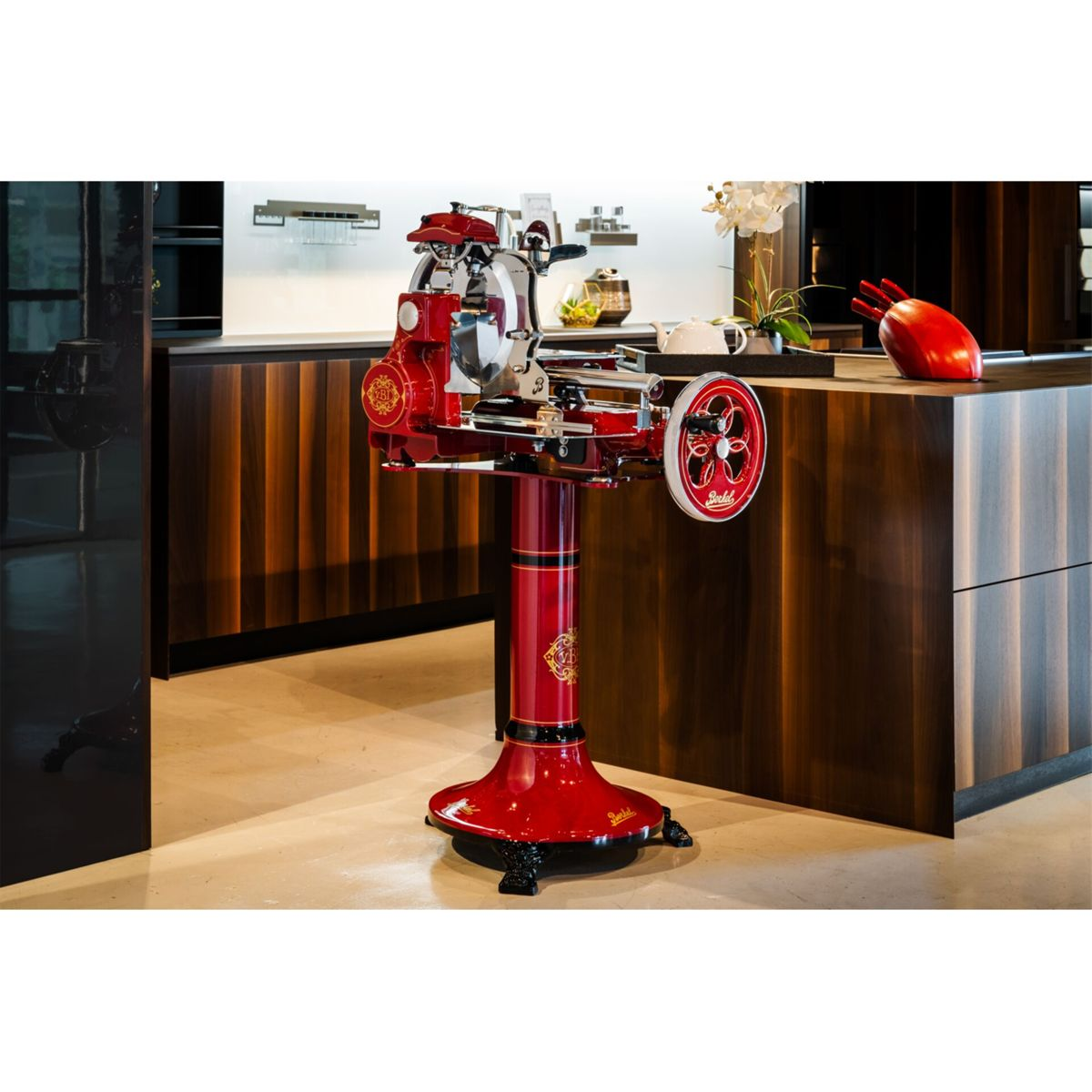 Ein roter Berkel-Aufschnittmaschine auf einem Sockel in einer modernen Küche.