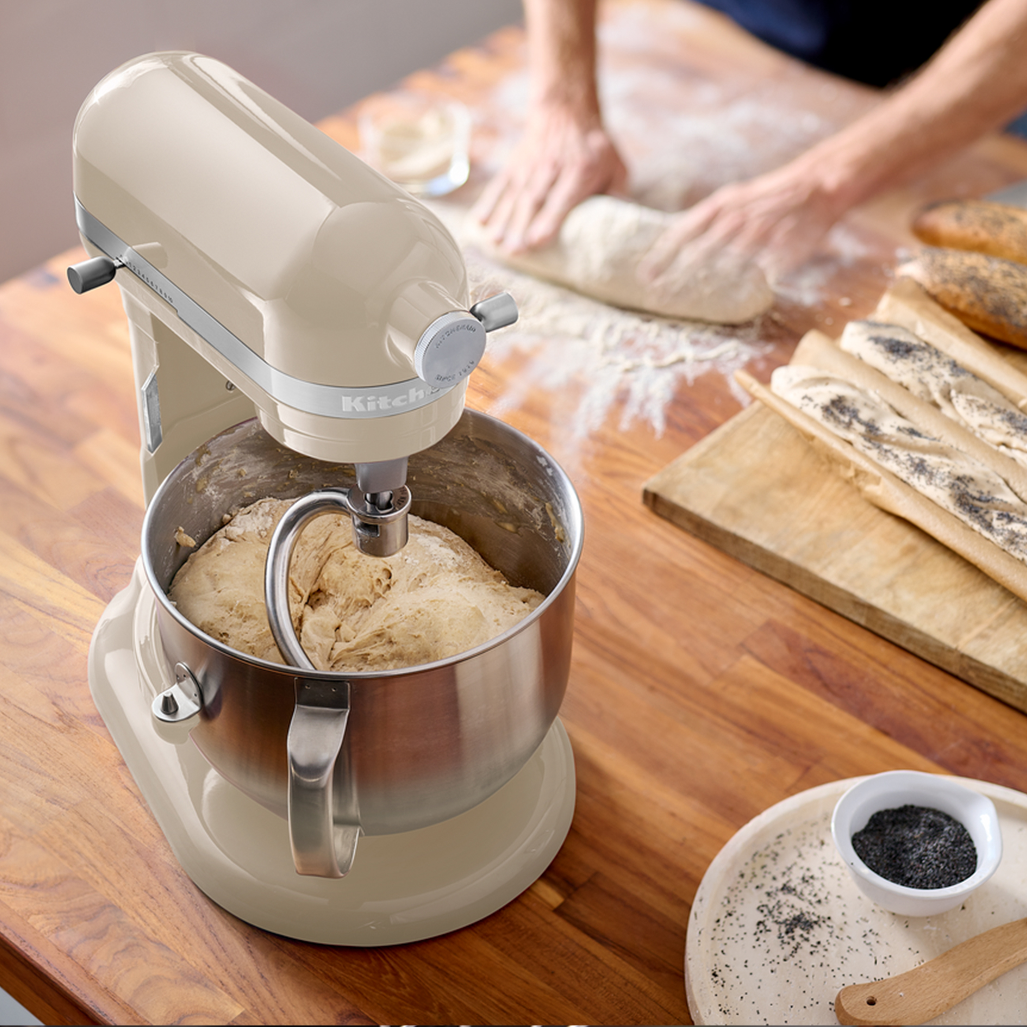 Un'impastatrice planetaria beige prepara l'impasto in una ciotola d'acciaio inox su un tavolo di legno.