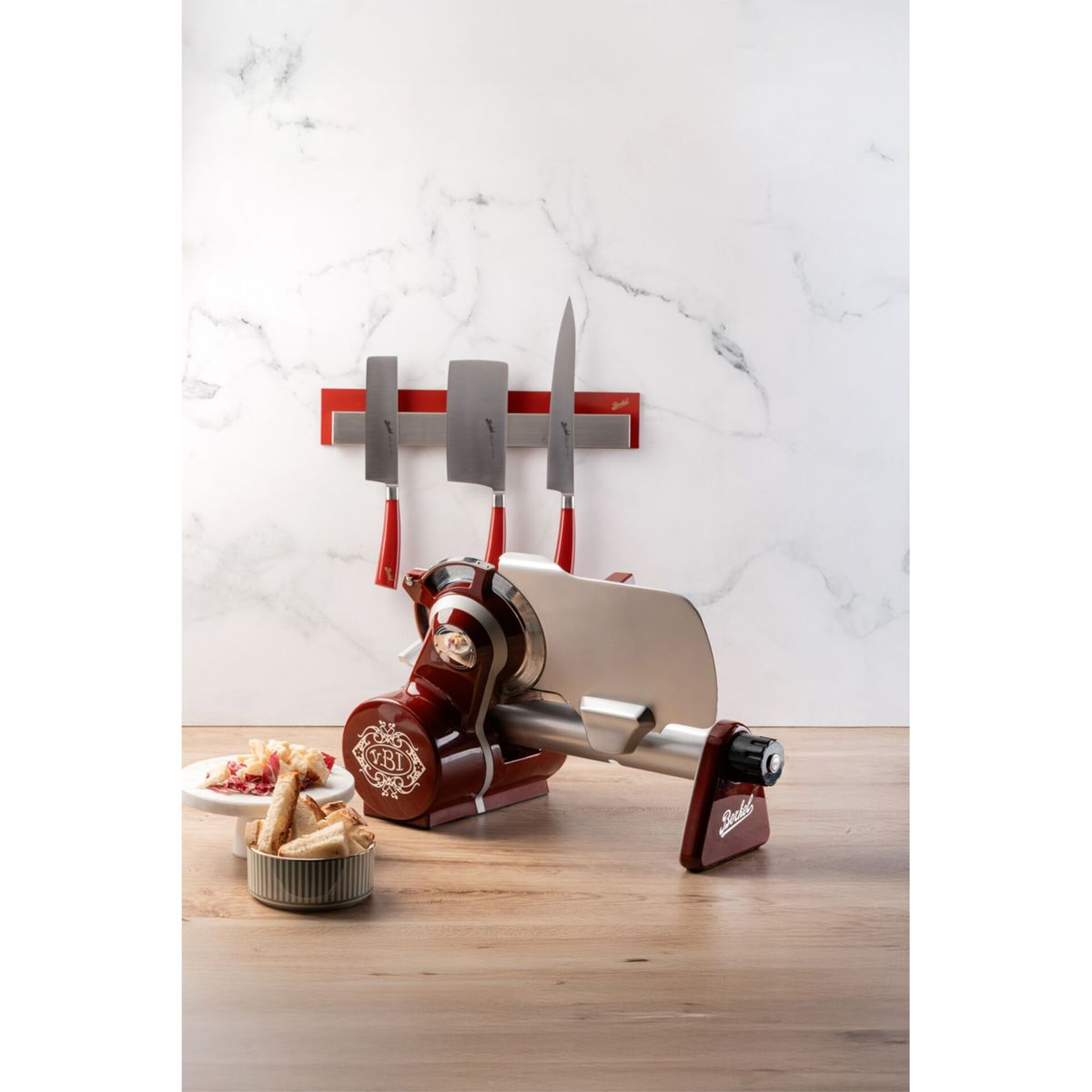 Una affettatrice di carne rossa con coltelli su una striscia magnetica a muro.