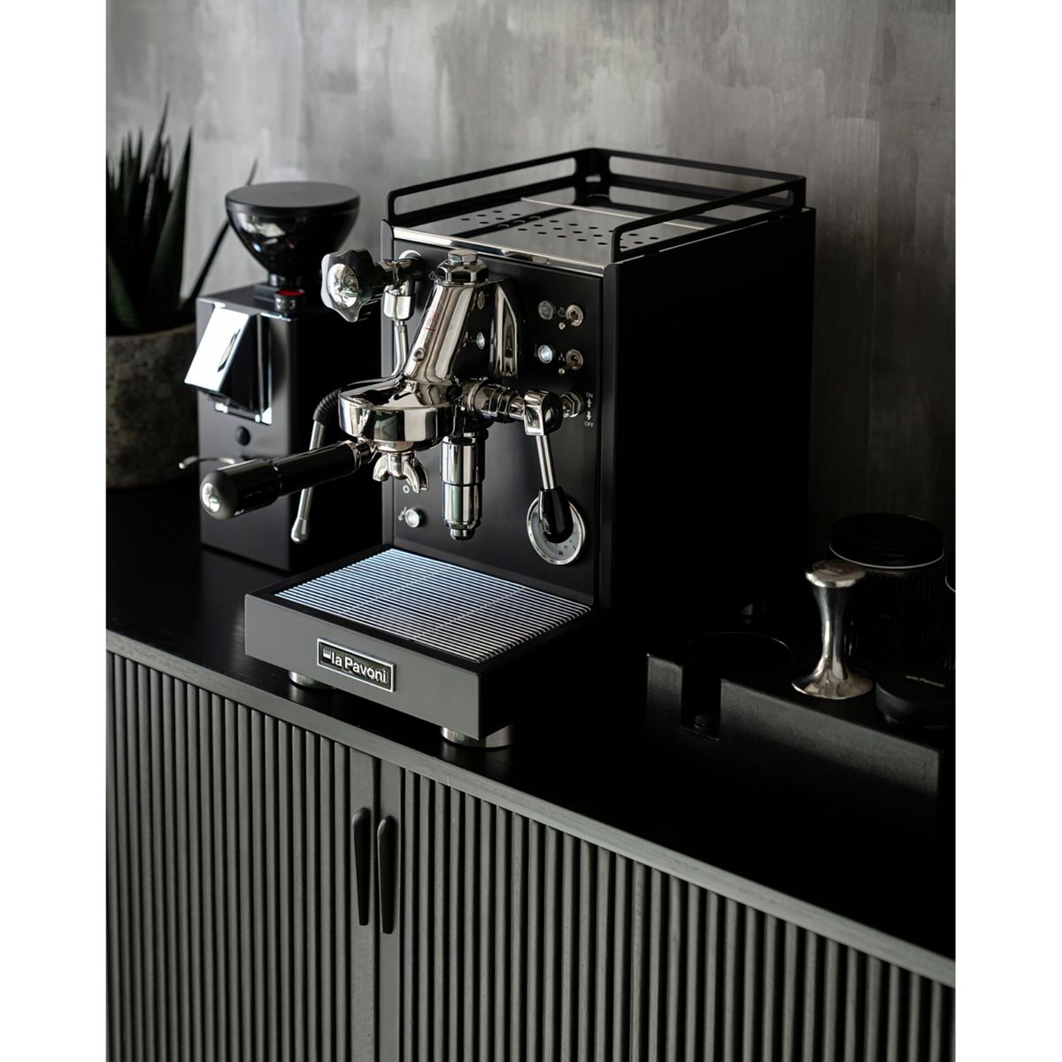Eine schwarze Espressomaschine mit Chromdetails steht auf einem schwarzen Schrank.