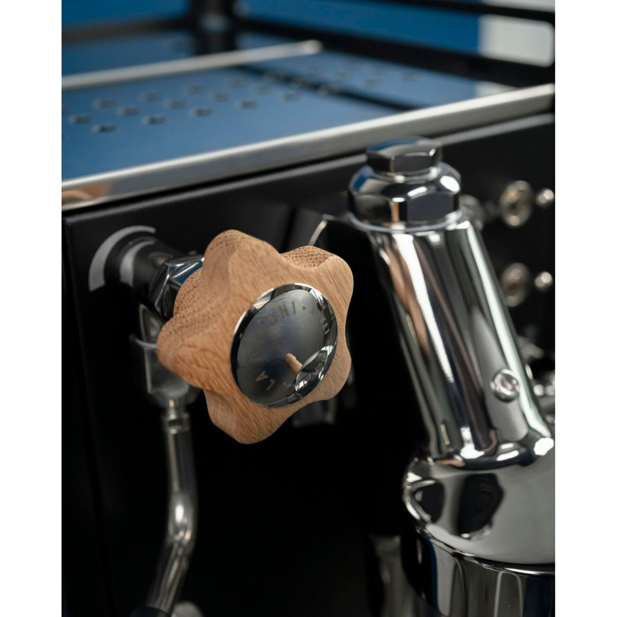 Nahaufnahme eines sternförmigen Holzknopfs und eines Chromhebels auf einer schwarzen Espressomaschine.