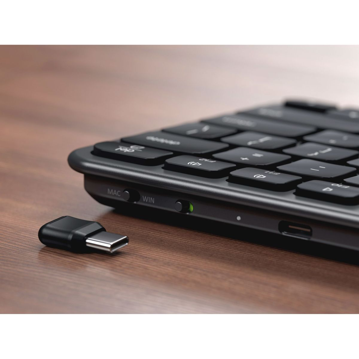 Ein schwarzer USB-C-Dongle neben einer Tastatur mit beleuchtetem Schalter.