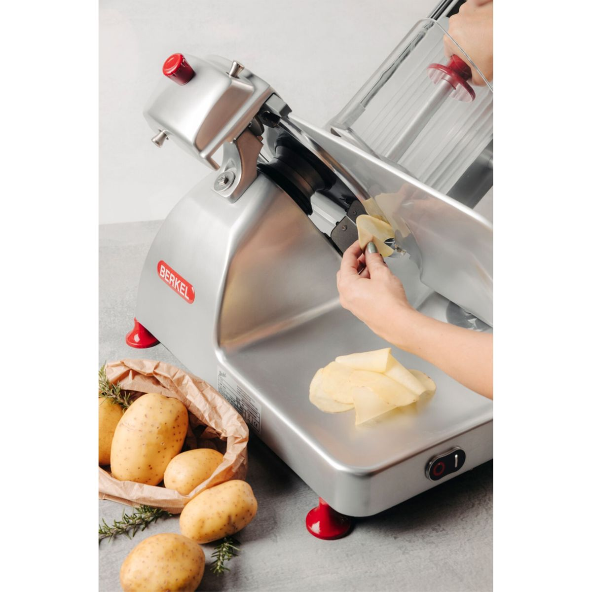 Eine Hand benutzt eine silberne Berkel-Maschine, um Kartoffeln zu schneiden.