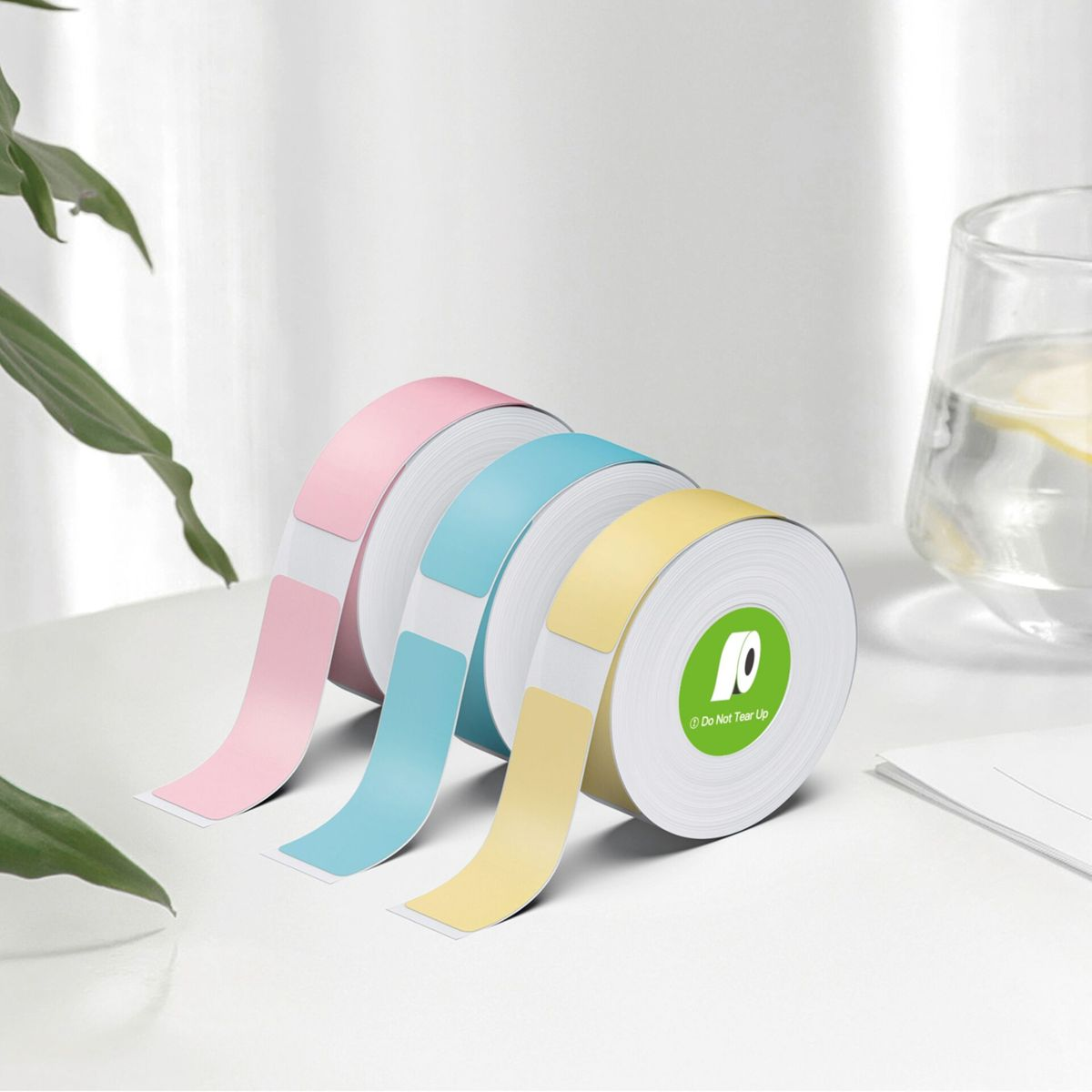 Drei Rollen mit bunten Etiketten: rosa, blau und gelb, auf einem weißen Tisch.