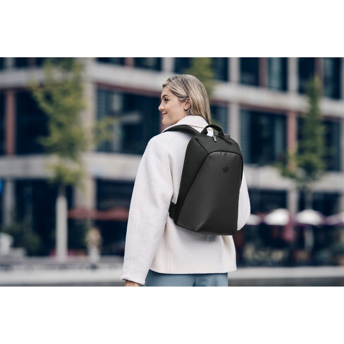 Frau im weißen Mantel trägt einen schwarzen Rucksack in der Stadt.