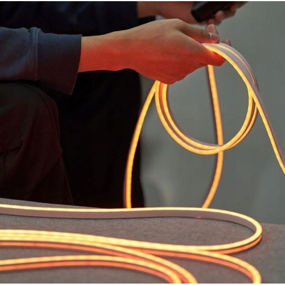 Ktoś trzyma świecący, pomarańczowy kabel neonowy. Jest ułożony na szarej powierzchni.