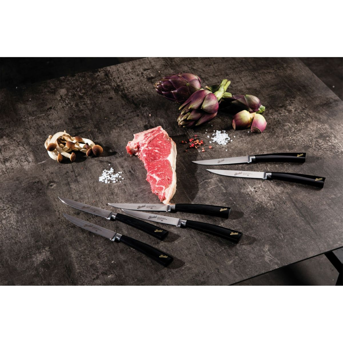 Ein rohes Steak, Pilze, Artischocken und Messer liegen auf einem Tisch.