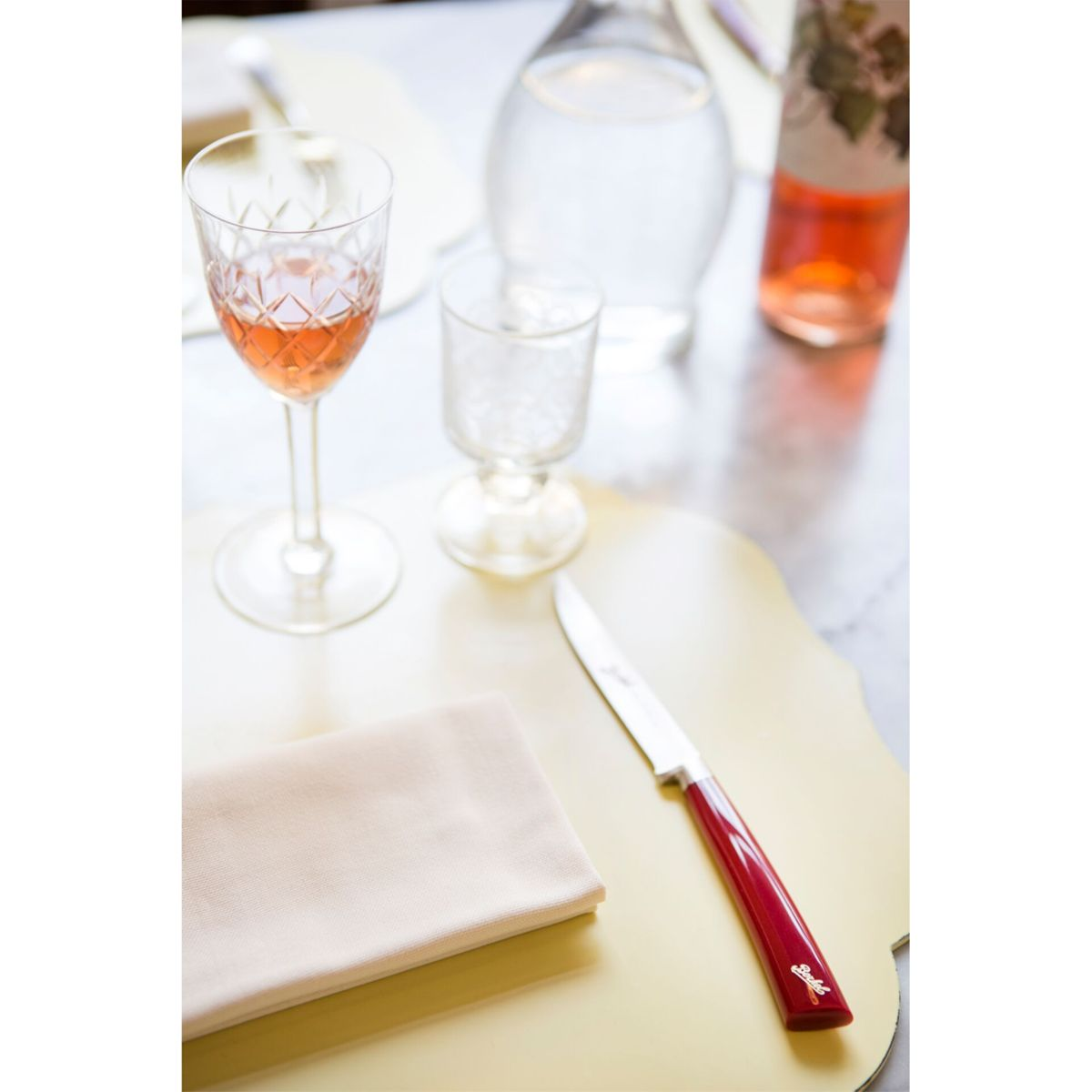 Ein Glas Rotwein, ein leeres Glas, eine Serviette und ein Messer auf einem Tisch.