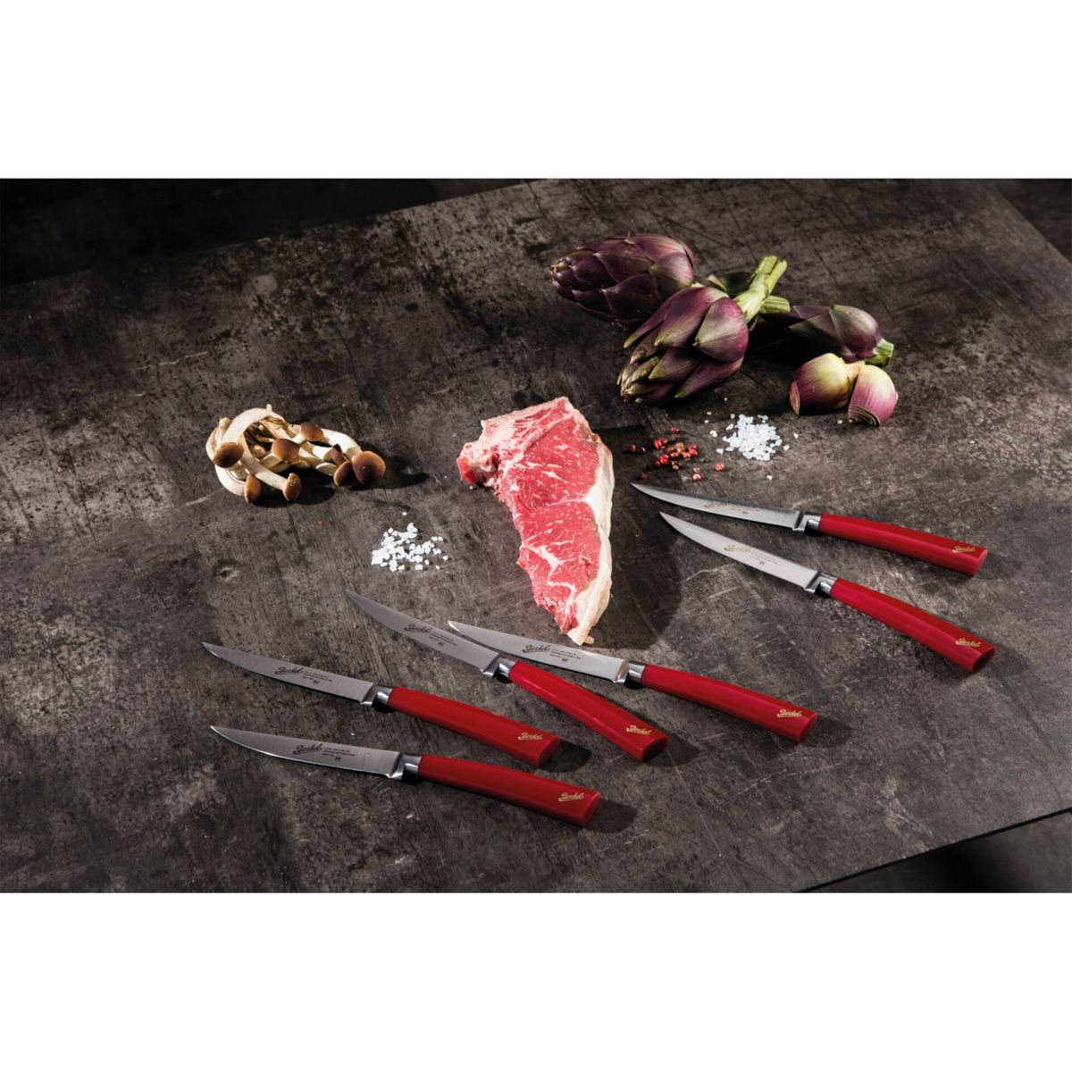 Ein rohes Steak, Pilze, Artischocken und Messer mit roten Griffen auf einem Holztisch.