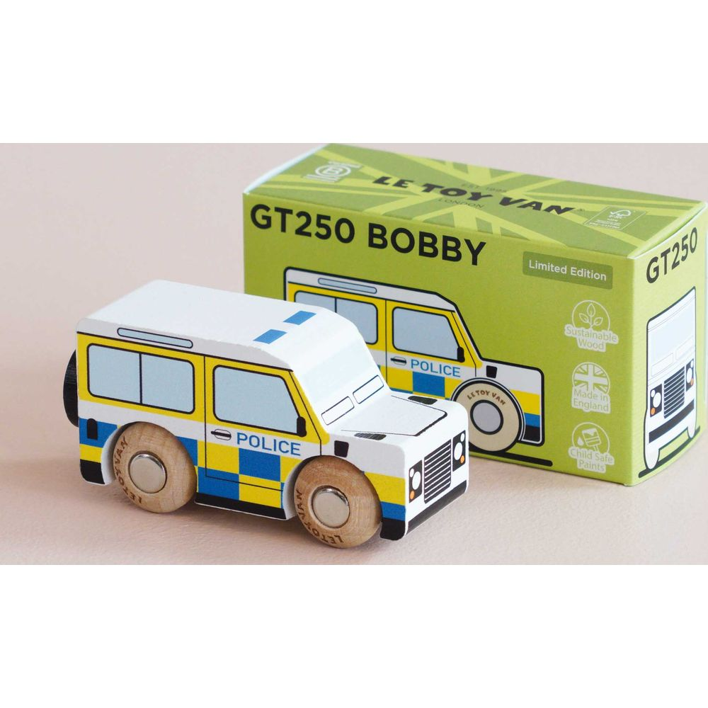 Ein weißes Spielzeugpolizeiauto mit gelben und blauen Karos, neben einer grünen Box.