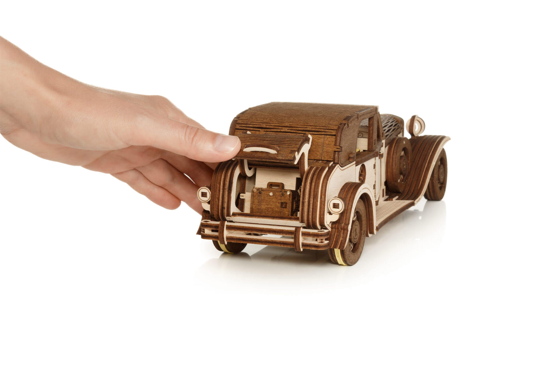 Eine Hand öffnet den Kofferraum eines hölzernen Oldtimer-Modells mit einem Koffer darin.