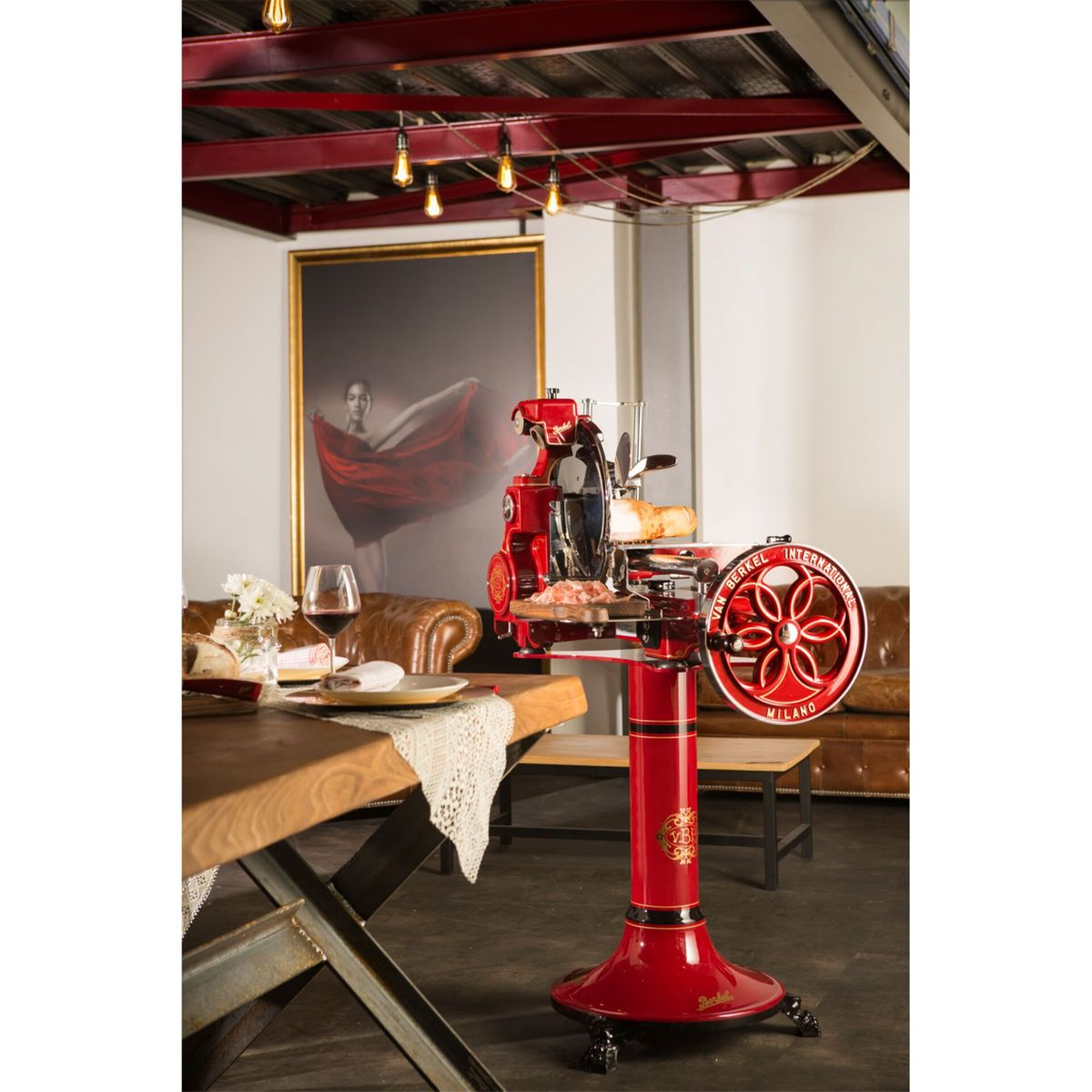 Ein roter Aufschnittschneider steht neben einem Holztisch mit Essen. Ein Kunstwerk im Hintergrund.