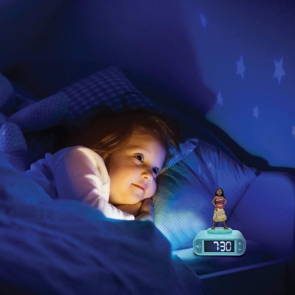 Un niño yace en la cama, una mesita de noche azul y una luz de alarma de Moana.