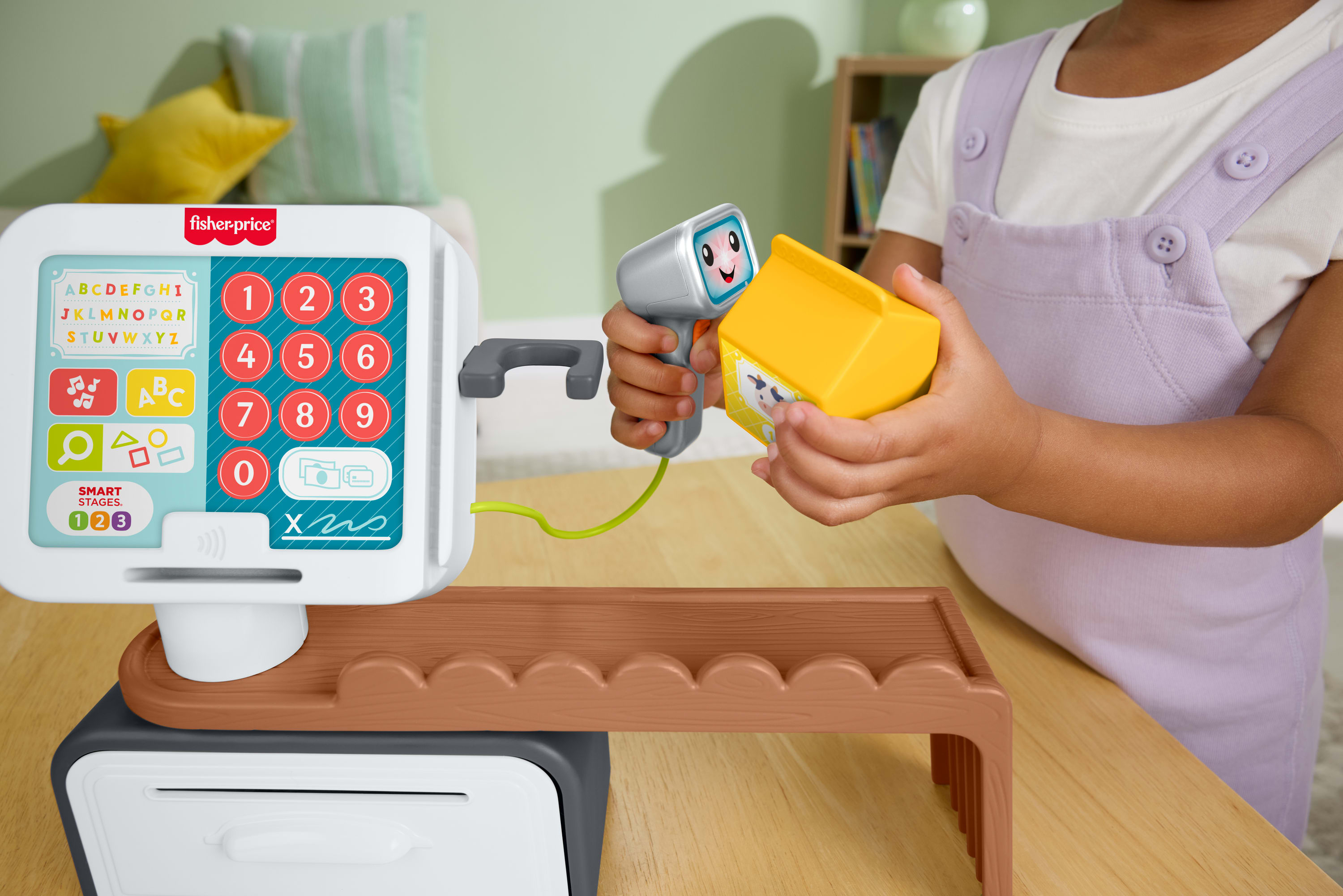 Ein Kind spielt mit einer Fisher-Price-Kasse, scannt eine gelbe Milchpackung.