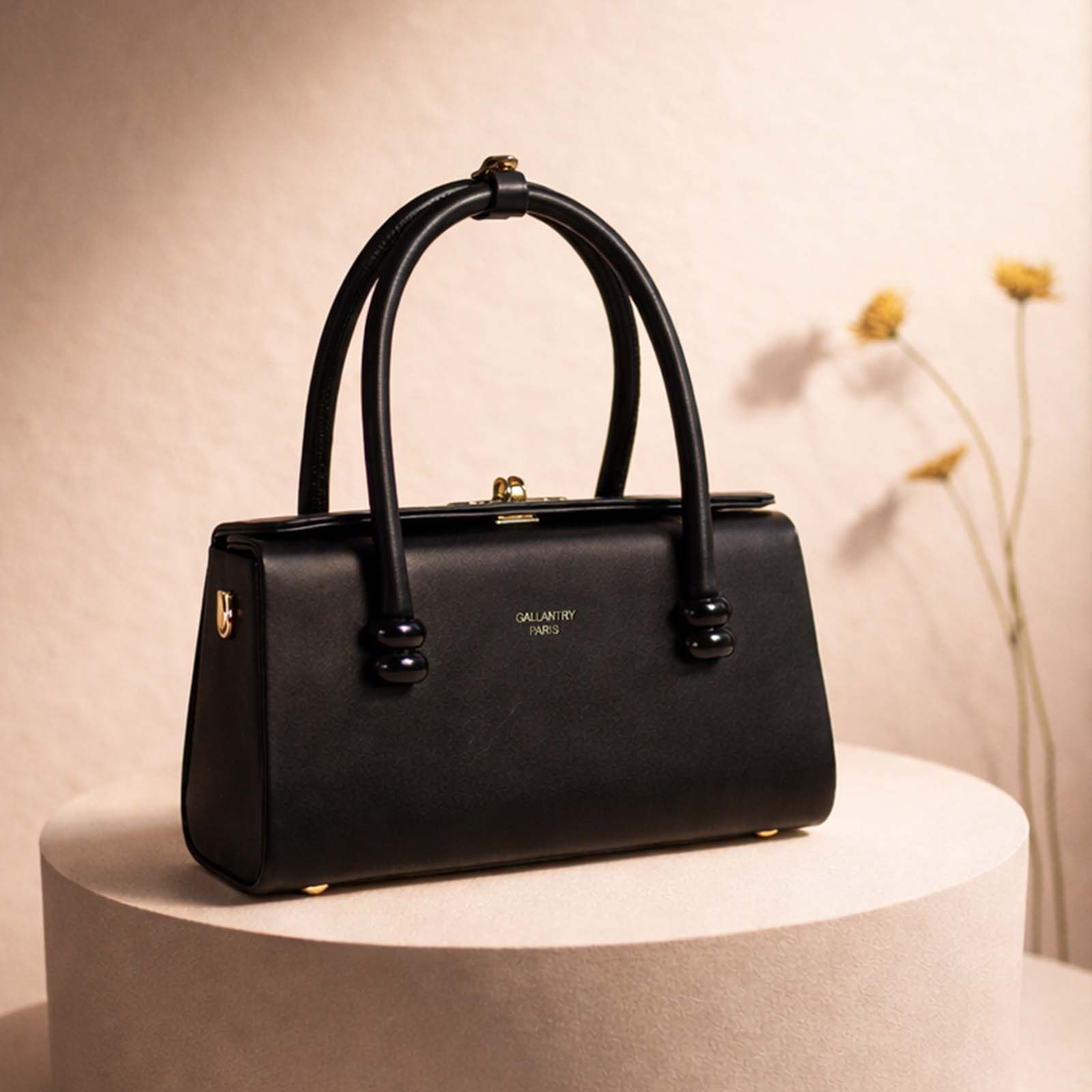 Bolso negro con detalles dorados sobre un pedestal, flores amarillas al fondo.