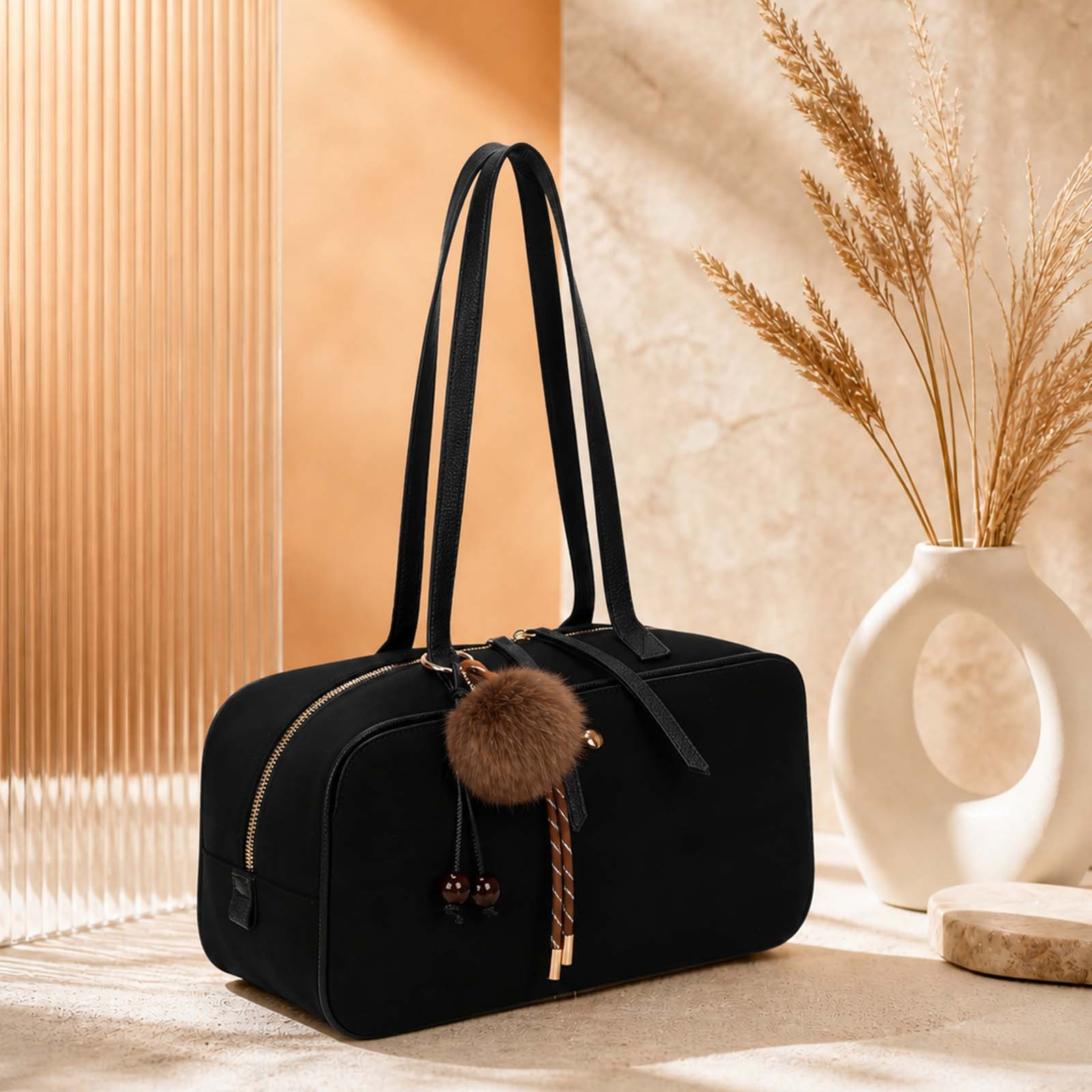 Bolso negro con charm de pompón, junto a un jarrón con hierbas secas.