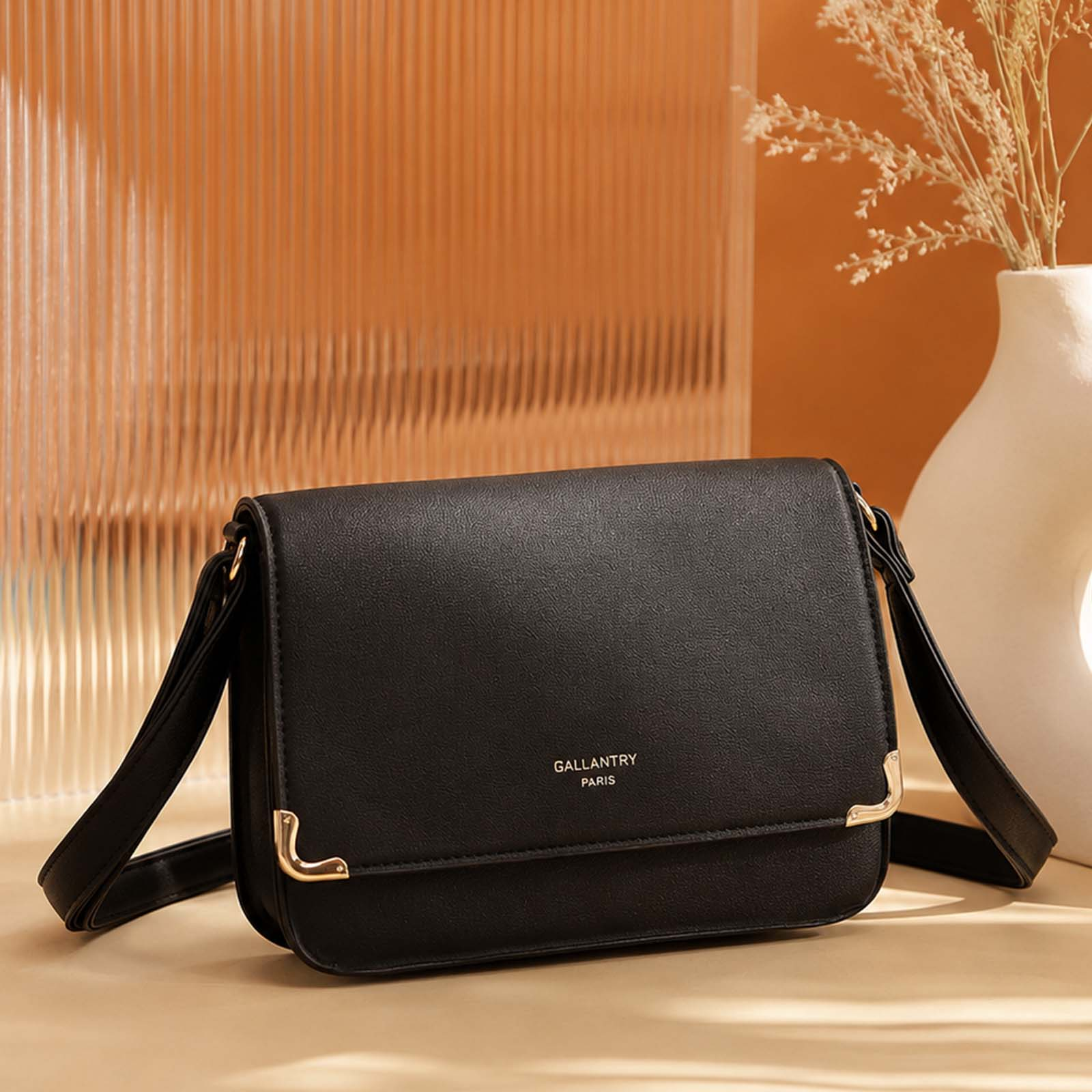 Un bolso cruzado negro con detalles dorados sobre una mesa.