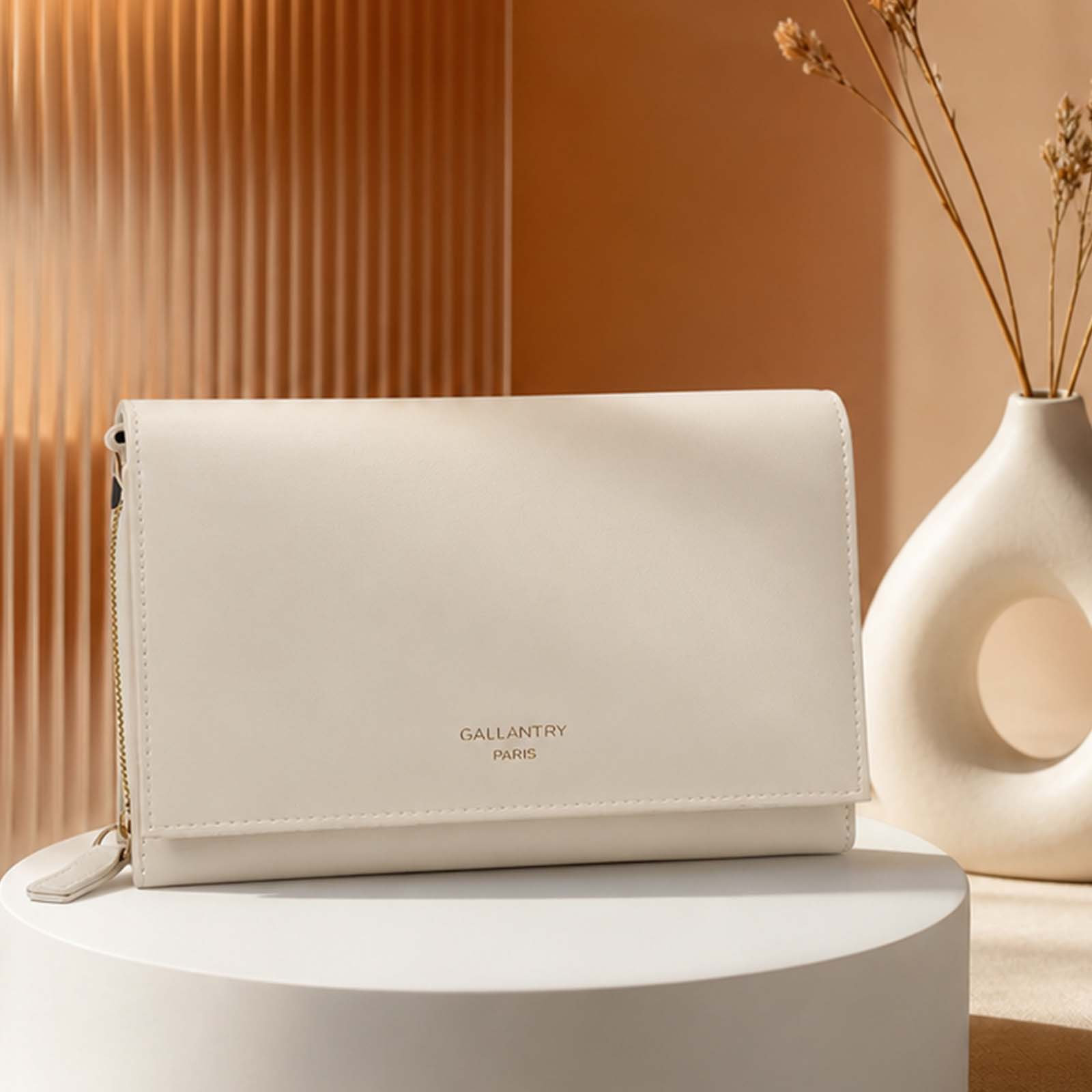 Una cartera color crema con herrajes dorados descansa sobre un pedestal blanco.