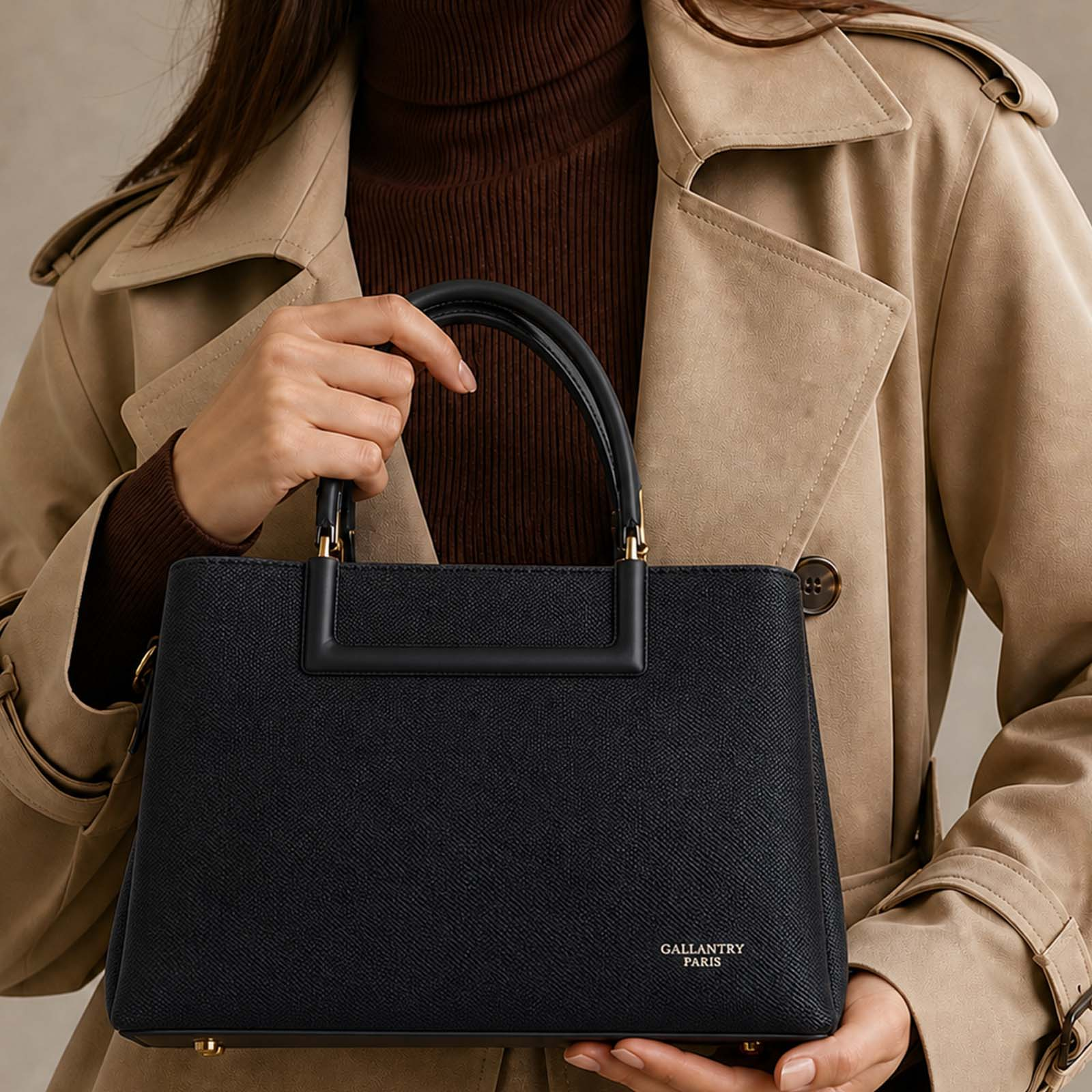 Una mujer sostiene un bolso negro, con jersey de cuello alto y gabardina beige.
