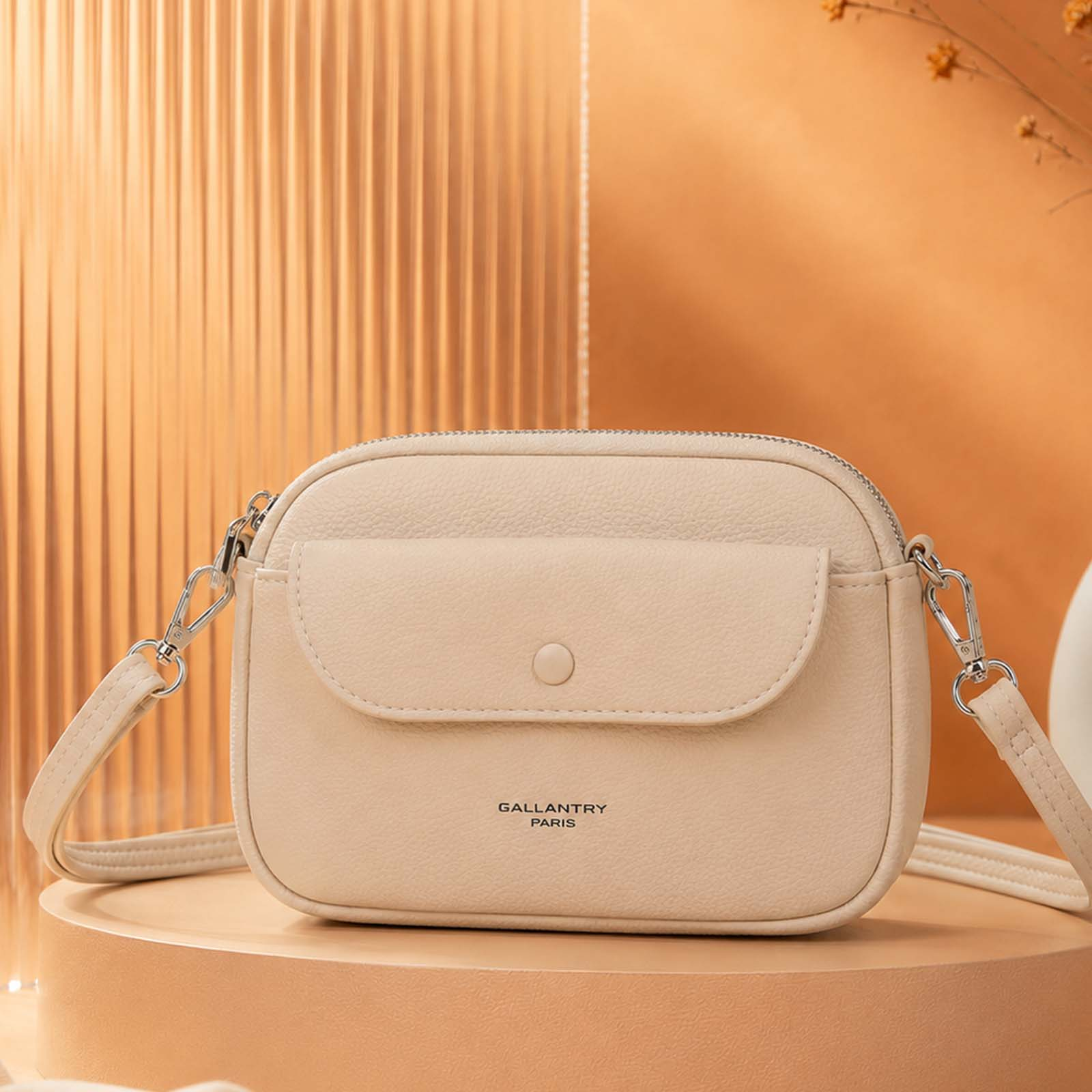 Bolso cruzado color crema con solapa y botón, expuesto sobre un pedestal.