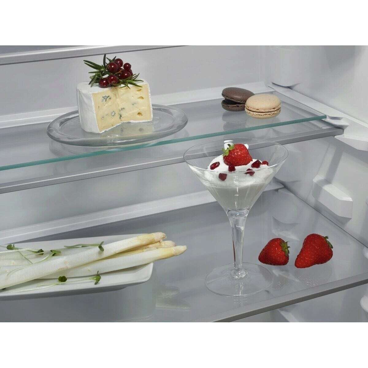 Formaggio, macaron, asparagi e dolce alle fragole in un frigorifero.