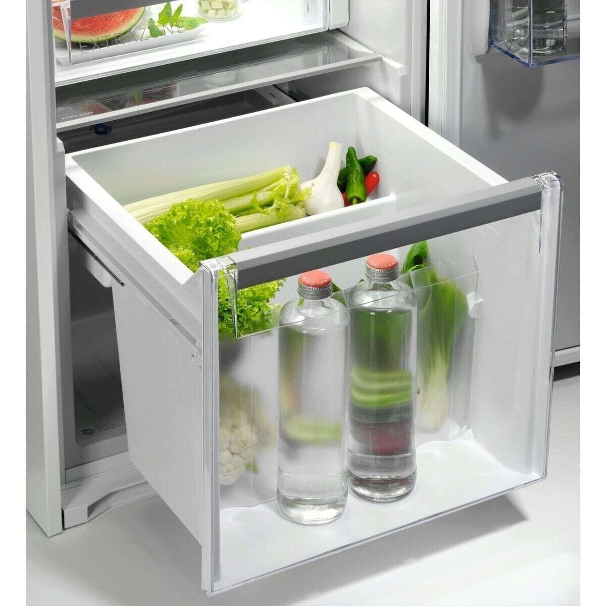 Cassetto verdure con lattuga, sedano, aglio, peperoncini, cavolfiore e bottiglie d'acqua.