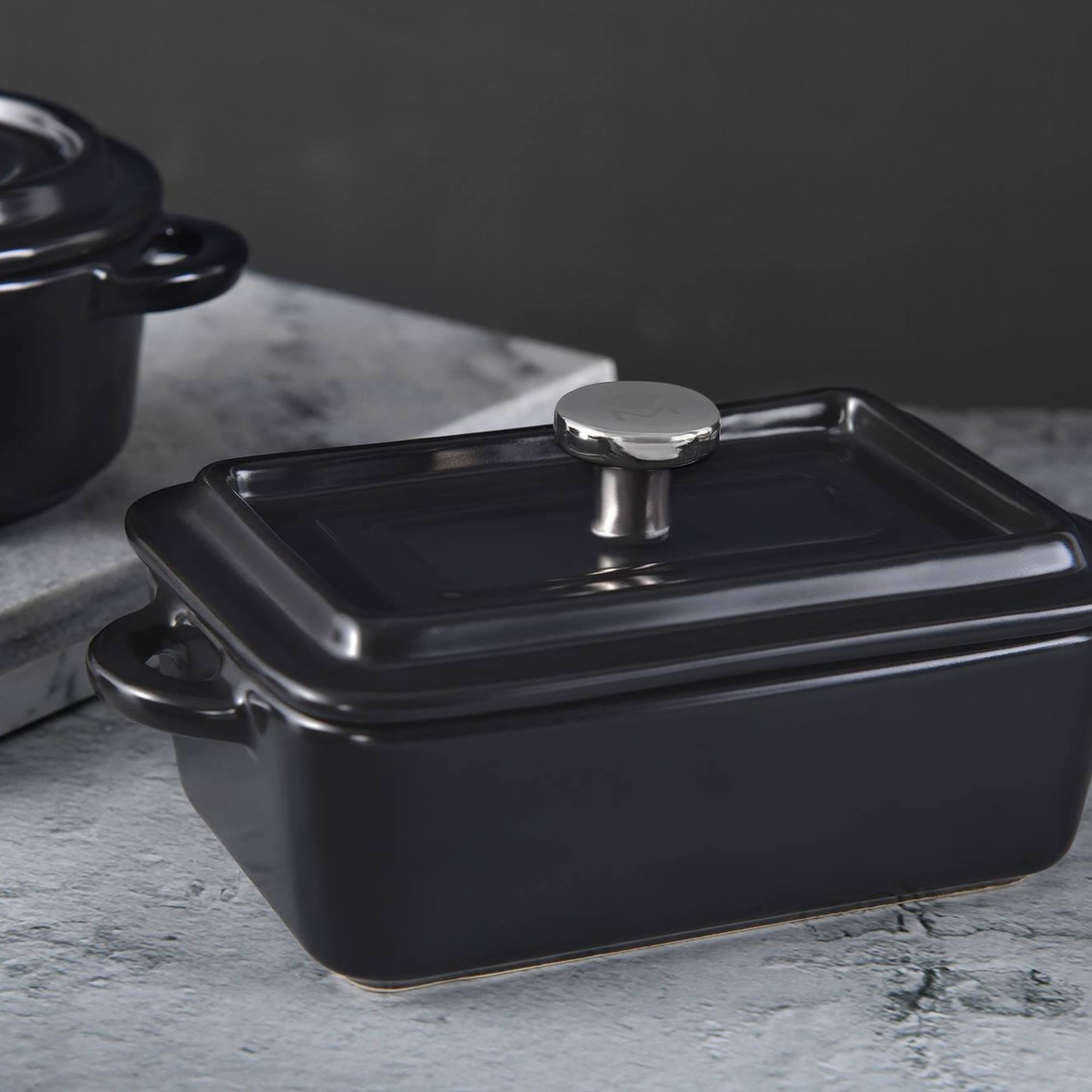Una olla rectangular de cerámica negra con asa plateada sobre superficie de mármol.