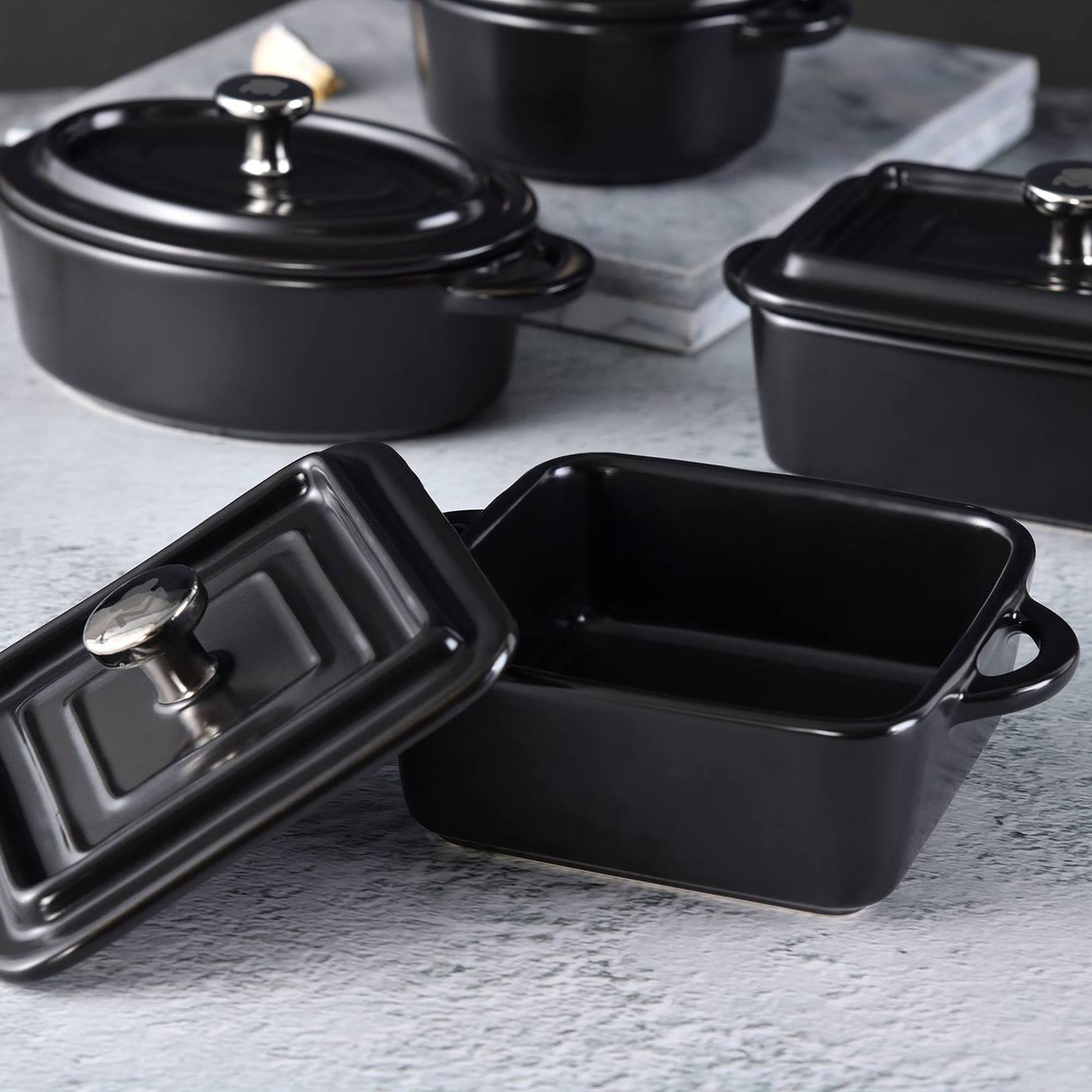 Varias cazuelas negras de cerámica con asas plateadas sobre una mesa.