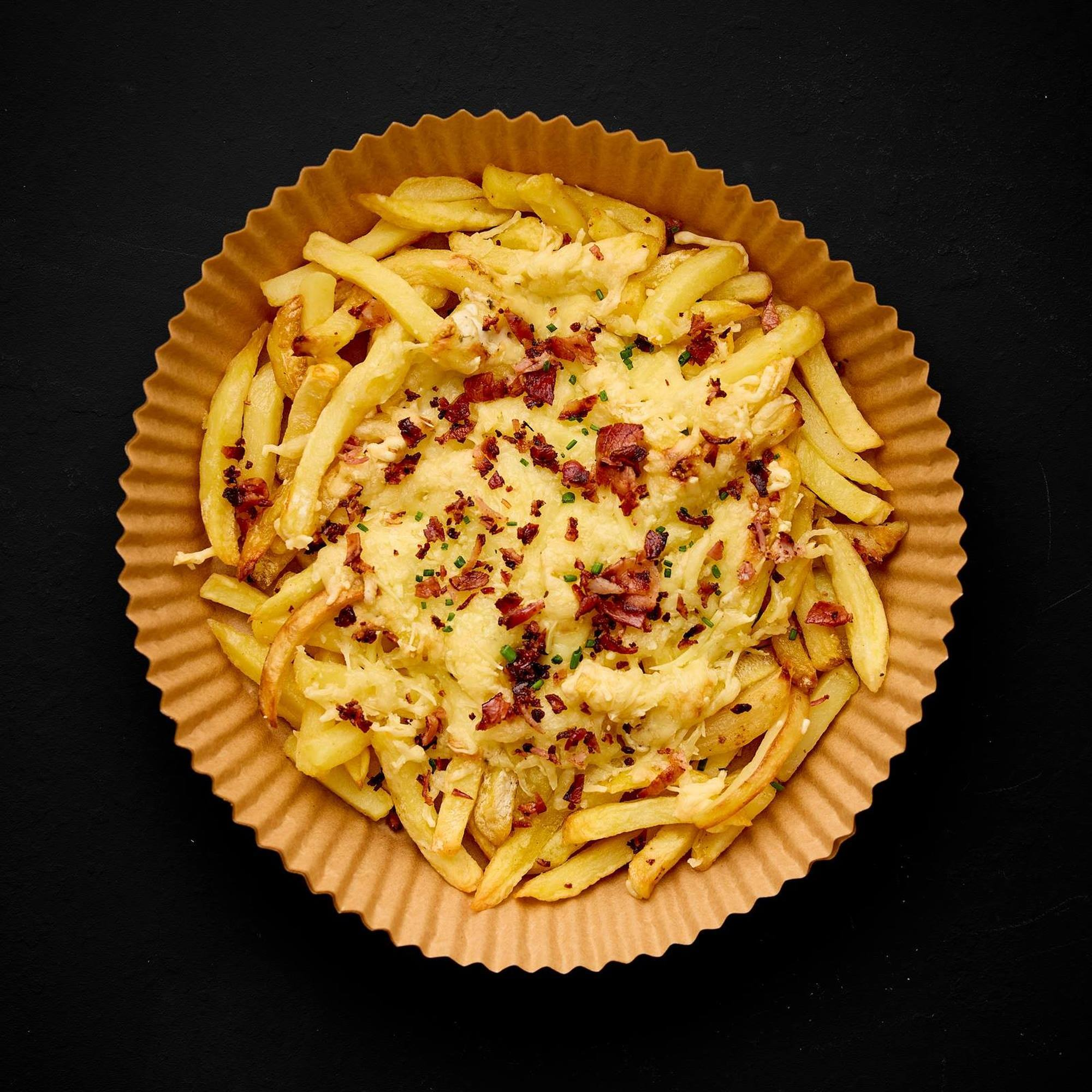 Papas fritas con queso y tocino en un revestimiento de papel marrón sobre fondo negro.