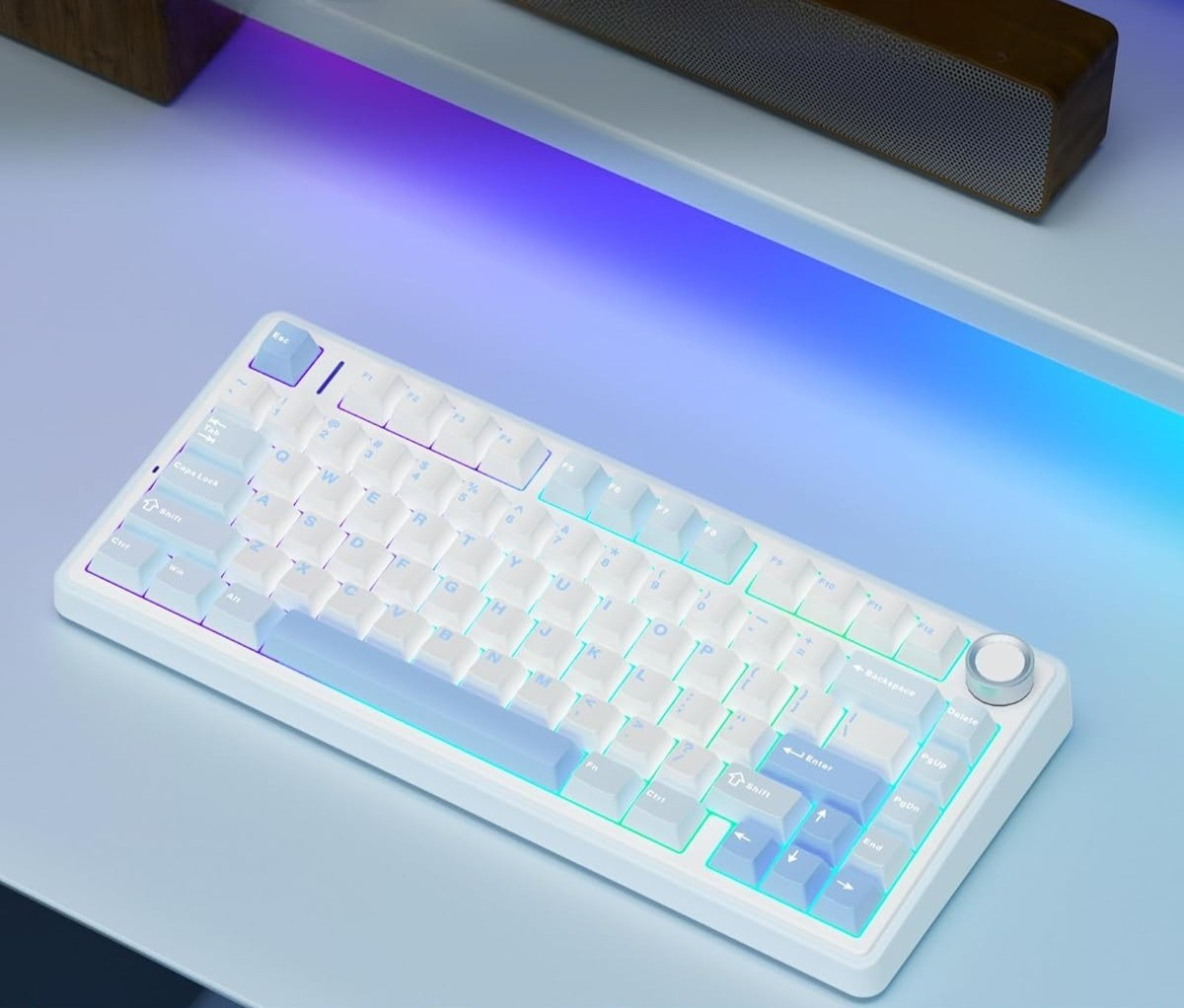 Biała klawiatura mechaniczna z podświetleniem RGB stoi na biurku, w tle drewniany głośnik.