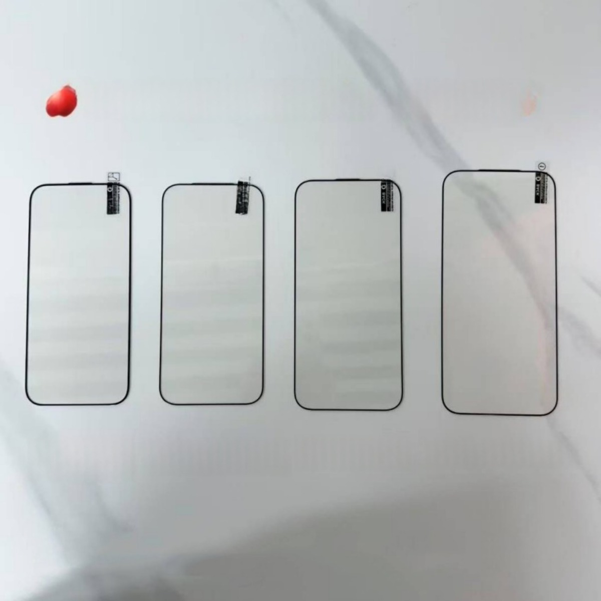 Quattro protezioni trasparenti per schermo di smartphone giacciono su marmo bianco.