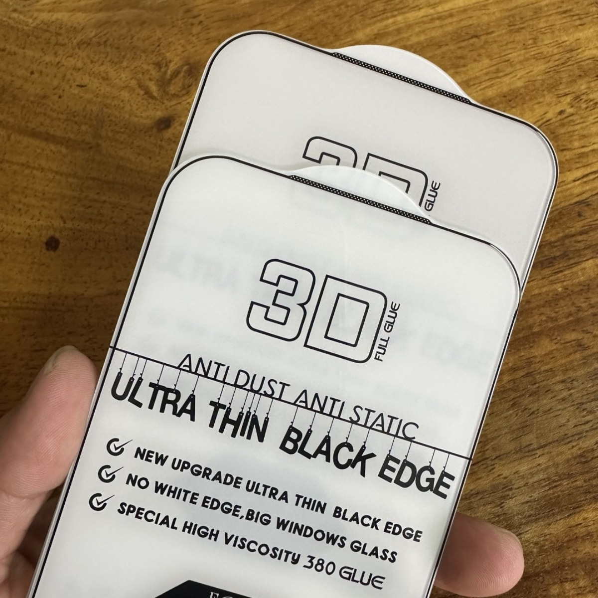 Due pellicole protettive per schermo di telefono con stampa "3D FULL GLUE" su tavolo legno.