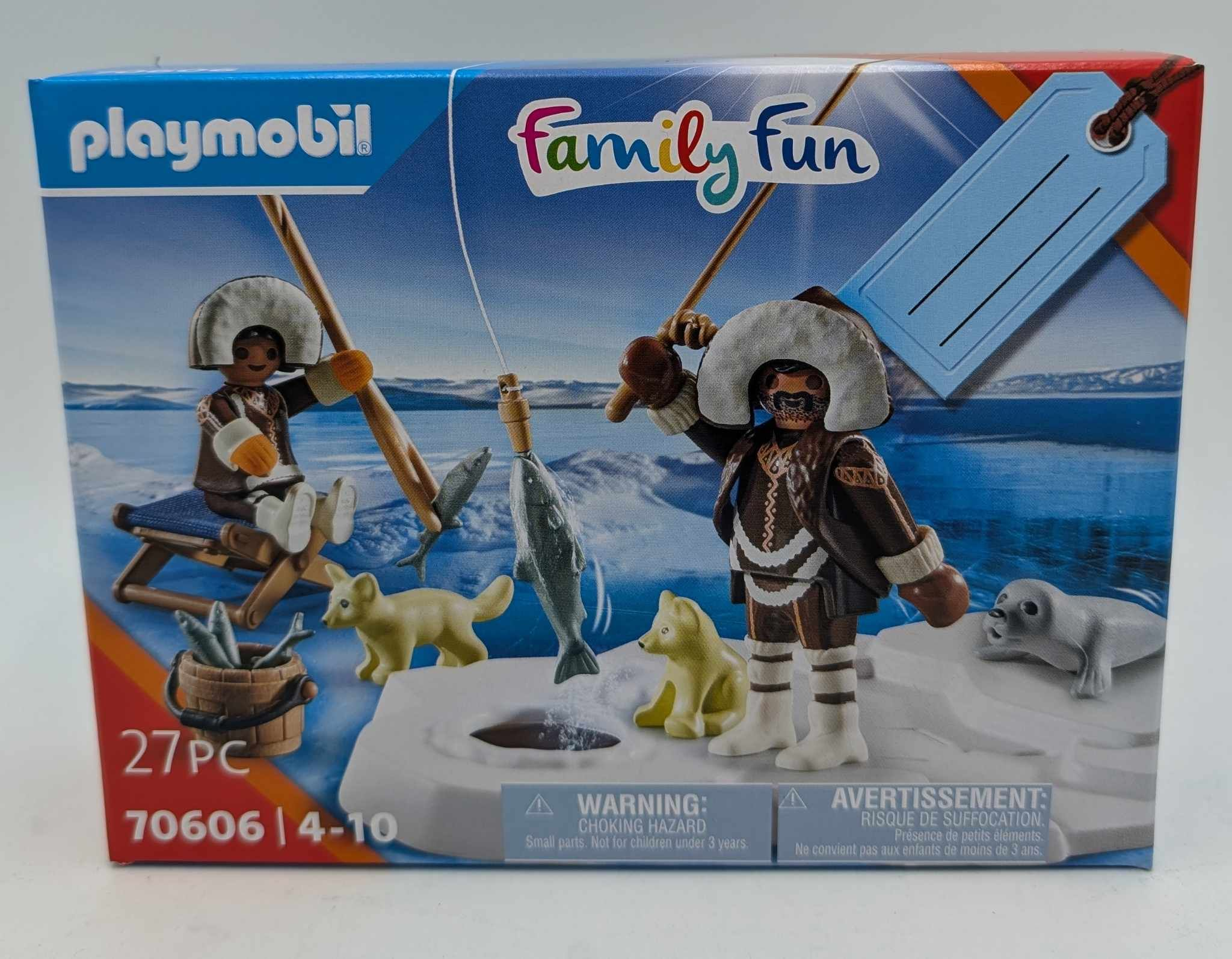 Playmobil Family Fun Box mit zwei Figuren beim Eisfischen, zwei Hunden, einer Robbe und einem Eimer voller Fische in einer Schneelandschaft.