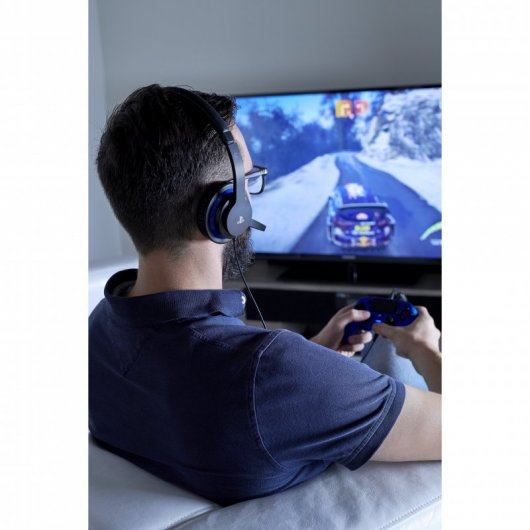 Una persona de espaldas, con auriculares, jugando un videojuego de carreras en una gran pantalla de TV con un controlador azul.