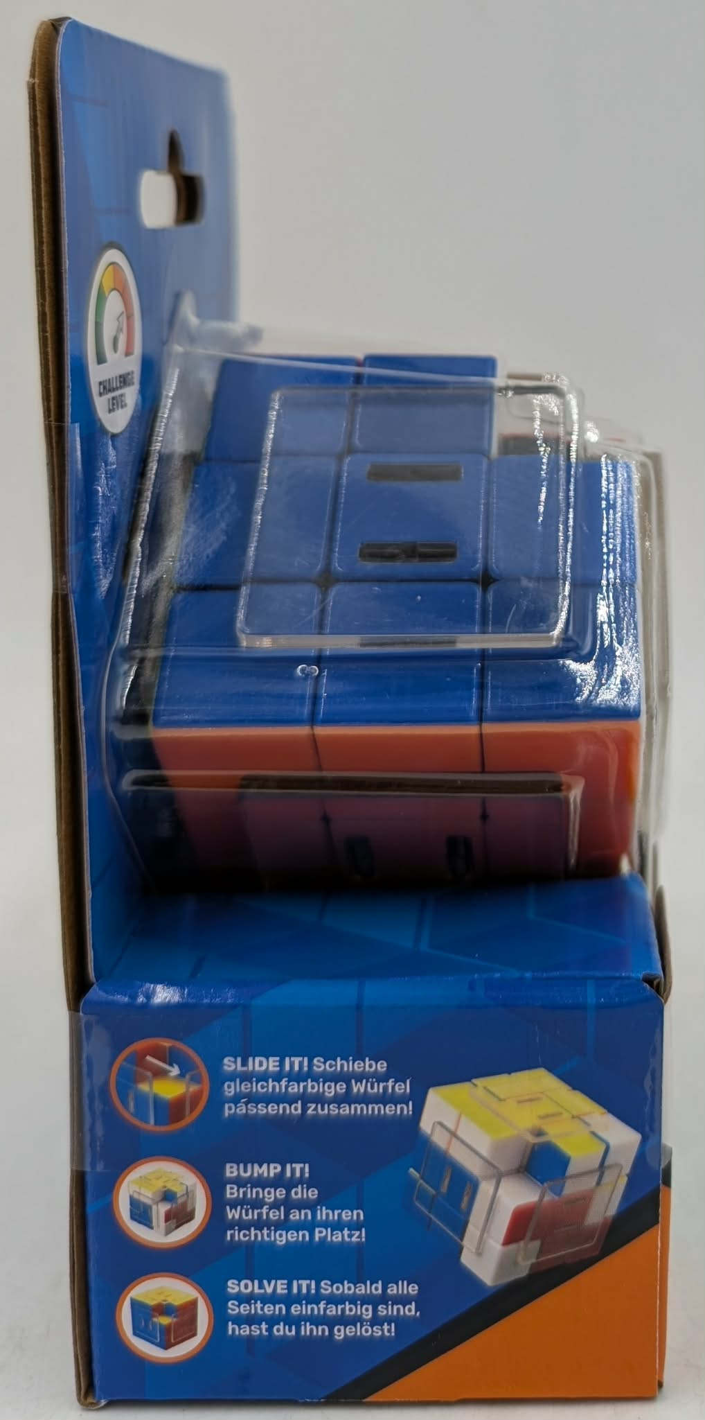 Ein verpacktes Rubik's-ähnliches Puzzle in Blau und Orange, mit Anleitungen auf Deutsch vor weißem Hintergrund.