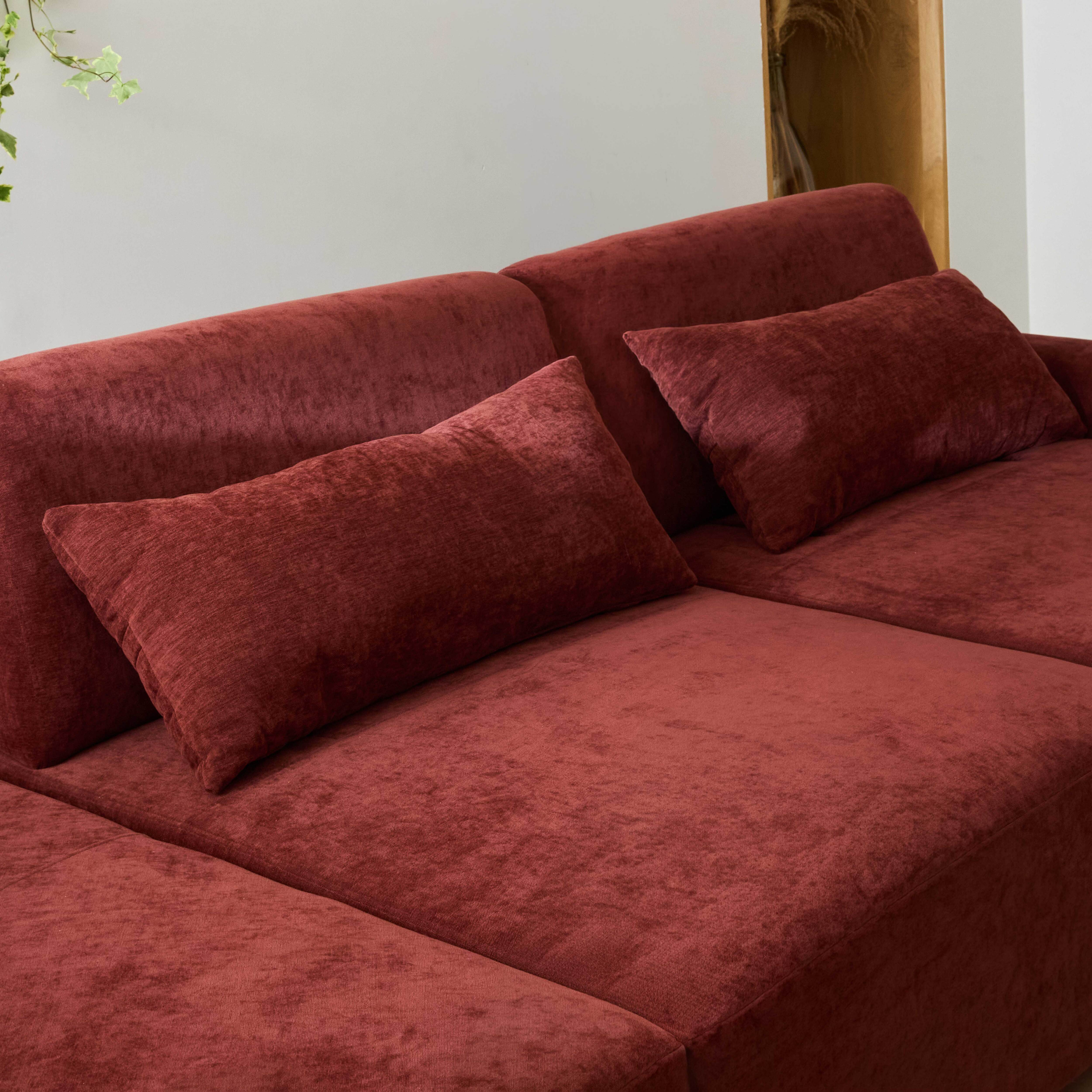 Ein rotes Ecksofa mit zwei Kissen und einer Pflanze im Hintergrund.
