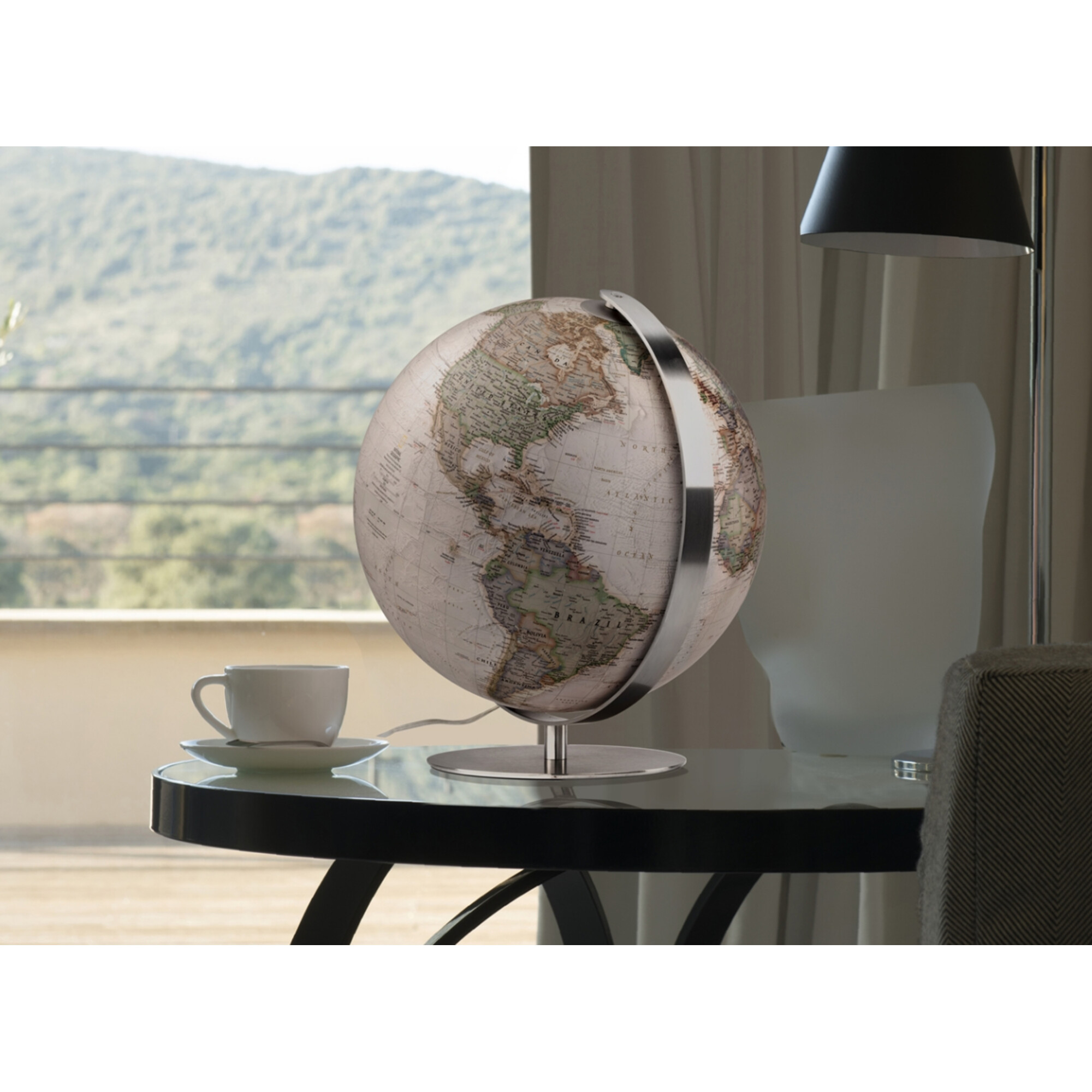Ein Globus mit einer Tasse Kaffee auf einem Tisch vor einem Fenster mit Berglandschaft.