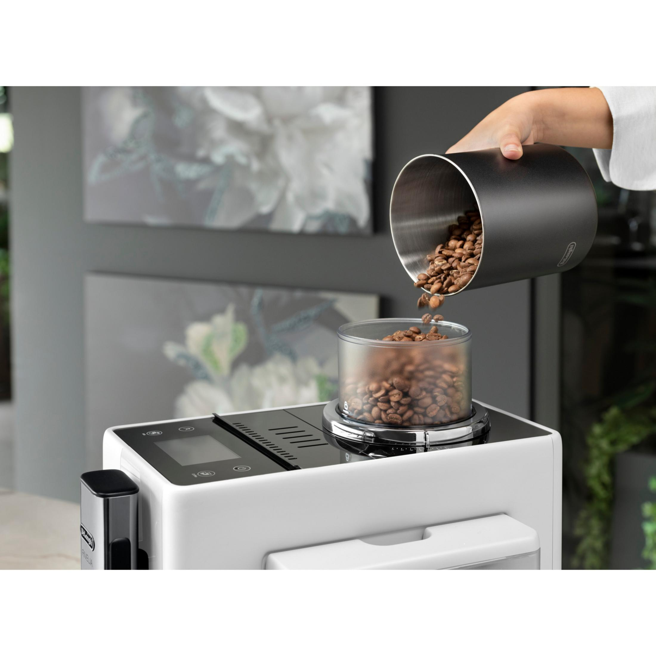 Eine Hand gießt Kaffeebohnen aus einem schwarzen Behälter in eine klare Mühle auf einer weißen Kaffeemaschine.